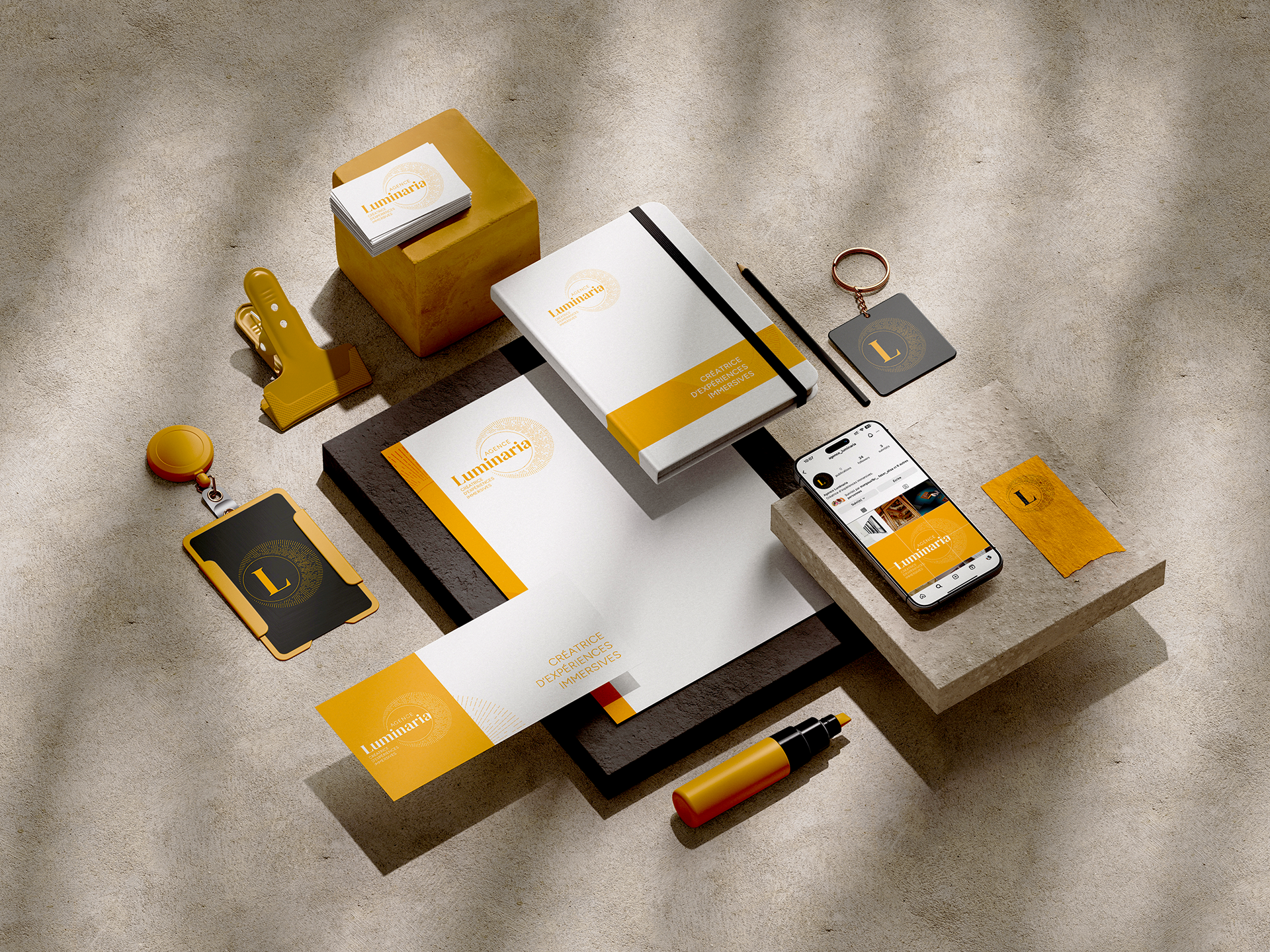 Papeterie d'entreprise et accessoires, dont des cartes de visite, un smartphone affichant un site, un carnet, un badge, une pince à papier, et un marqueur, sur fond texturé.