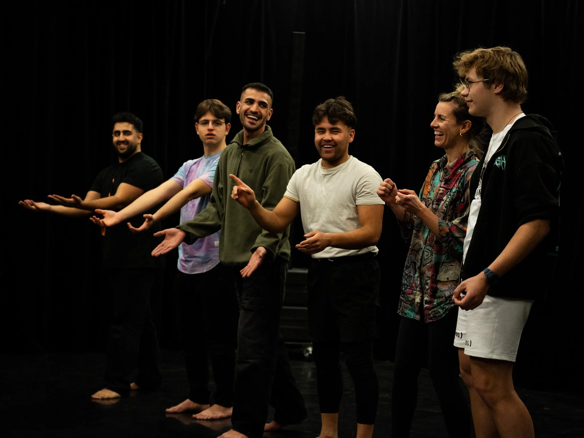 Menschen stehen in einer Reihe auf einer Bühne, lachen und unterhalten sich.