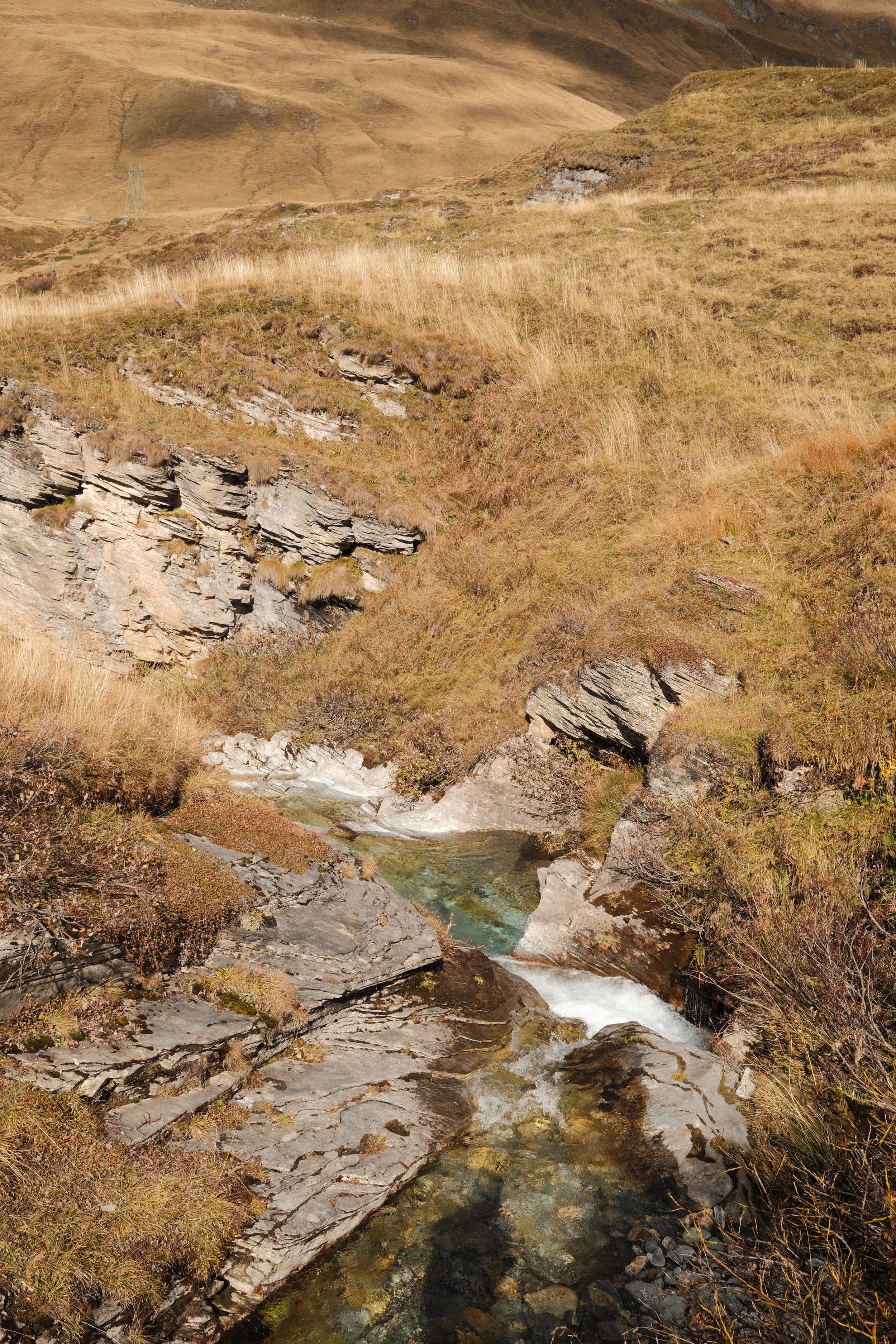 Landschaft mit einem kleinen Fluss, felsigen Ufern und hügeliger, grasbedeckter Umgebung in einer bergigen Region.