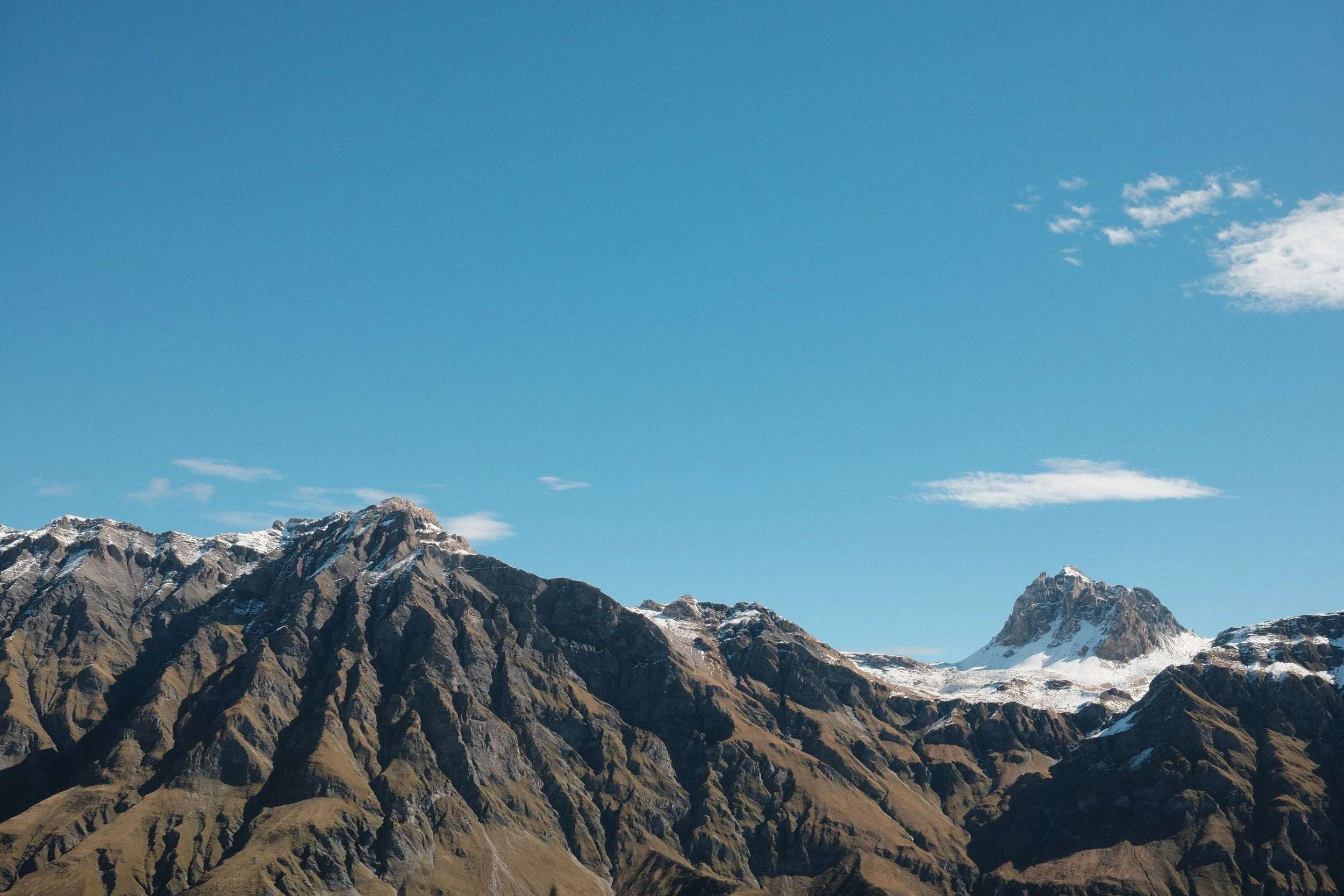 Bergkette mit schneebedeckten Gipfeln und blauem Himmel im Hintergrund.