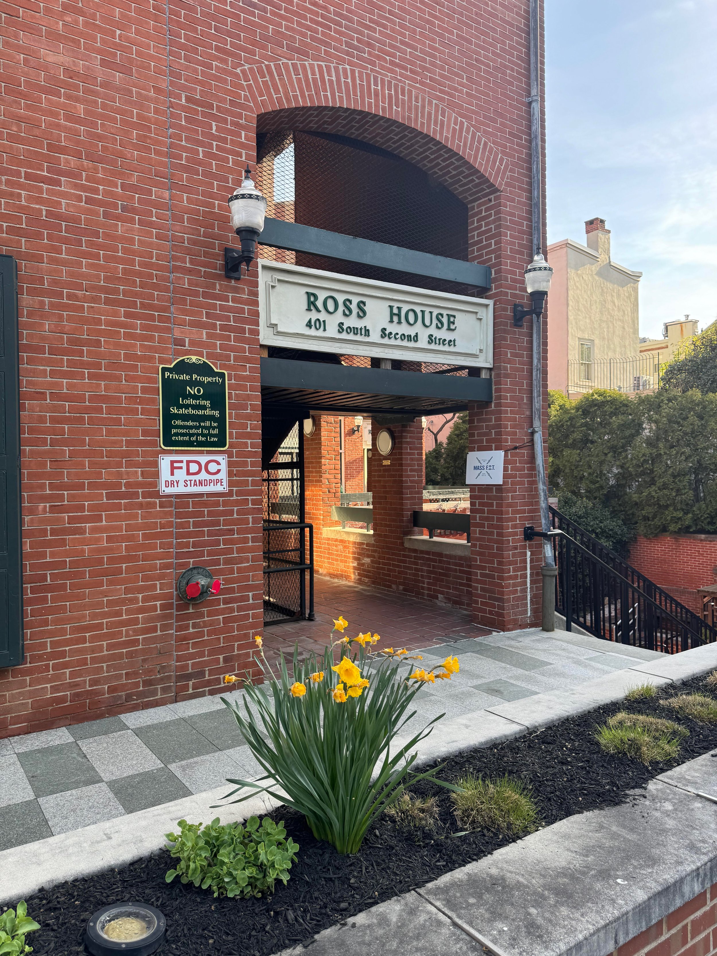 Main entrance for Luna Therapy Group. It is a brick building with a sign that reads Ross House, 401 South Second Street. There is a small garden with yellow flowers and green plants in the foreground, and a black metal railing beside a staircase.