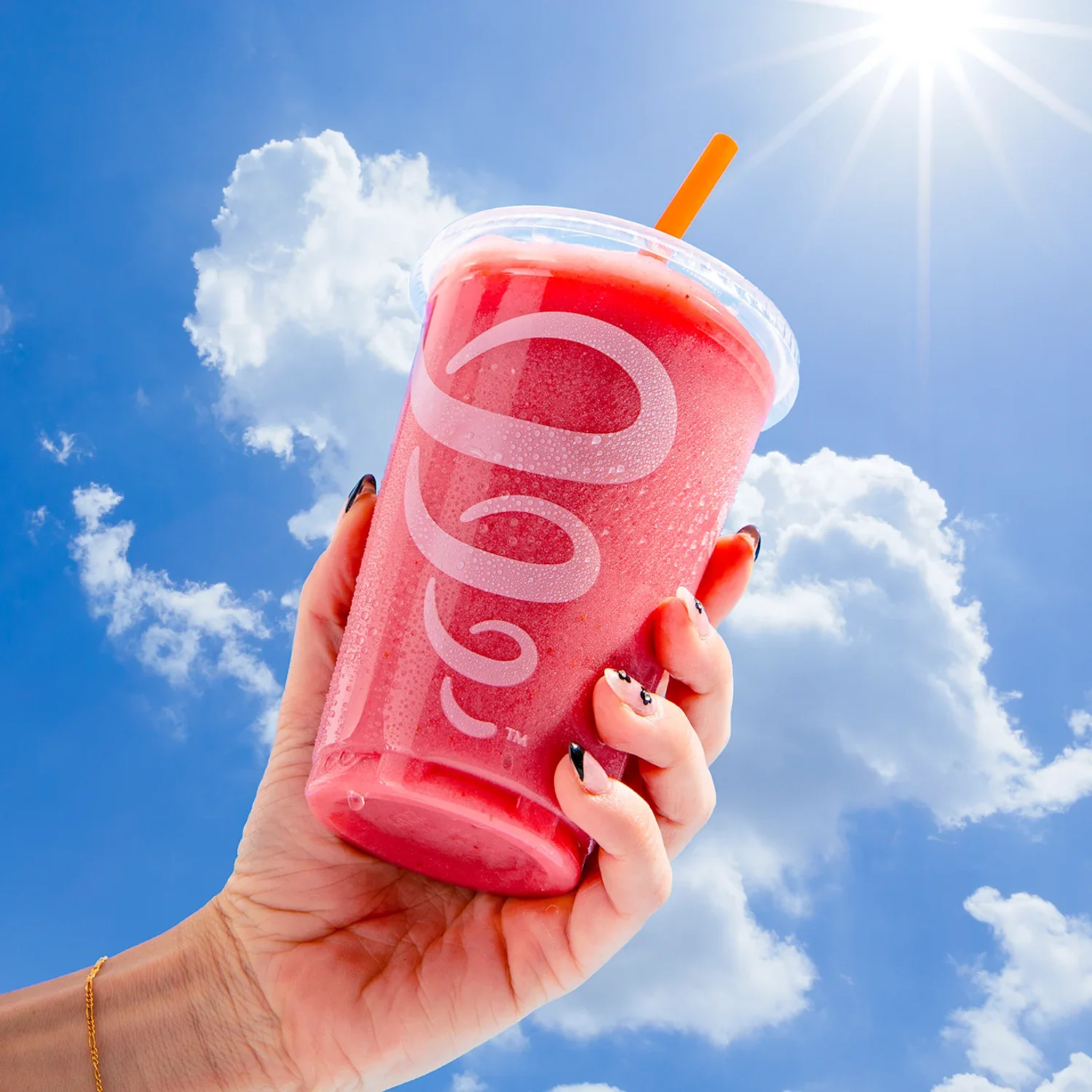 A pink smoothie in a cup with blue skies in the background