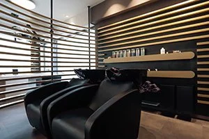 Innenraum eines Friseursalons in Bad Oeynhausen, HairClub mit schwarzen Liegen, Holzregalen und großen Fenstern mit horizontalen Jalousien.