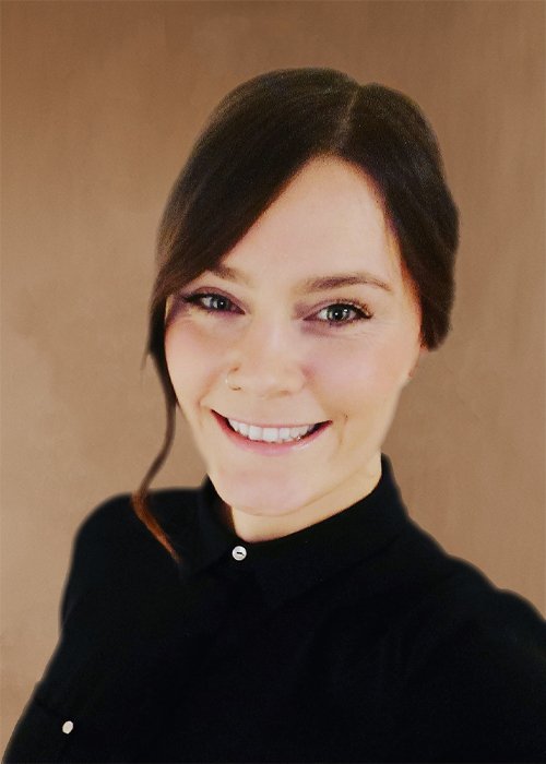 Eine Frau mit gesunden braunen Haaren, das lächelt, trägt ein schwarzes Hemd vor einem braunen Hintergrund. Charline Borcherding ist Top Stylistin/Friseurin im HairClub Bad Oeynhausen.