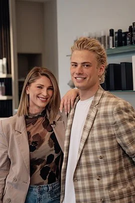 Nico Kallisch und Denis Sabur, Co-CEOs und Gründer vom Friseursalon HairClub Bad Oeynhausen stehen lächelnd im Salon und lächeln in die Kamera.