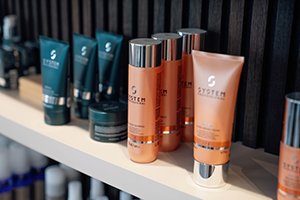 Pflegeprodukte in Tuben und Flaschen auf einer weißen Regalfläche von System Professional by Wella. Professionelle Haarpflege wird im Friseur Salon HairClub Bad Oeynhausen verkauft.