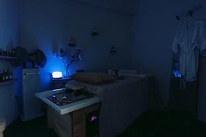 Ein dunkler Raum mit blauer Beleuchtung, Massageliege und Friseurwaschbecken – HeadSpa im HairClub Bad Oeynhausen. Im Friseursalon für Entspannung und gesunde, schöne Haare.