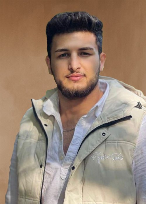 Junger Mann mit dunklem, gepflegtem Haar und Bart trägt eine helle Weste und ein weißes Hemd, steht vor einem braunen Hintergrund. Rinas Mohammad, Top Stylist und professioneller Friseur im HairClub Bad Oeynhausen.