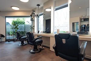 Innenansicht eines modernen Friseursalons in Bad Oeynhausen mit mehreren Friseurstühlen und großen Fenstern. Warme und helle Atmosphäre zum Wohlfühlen.