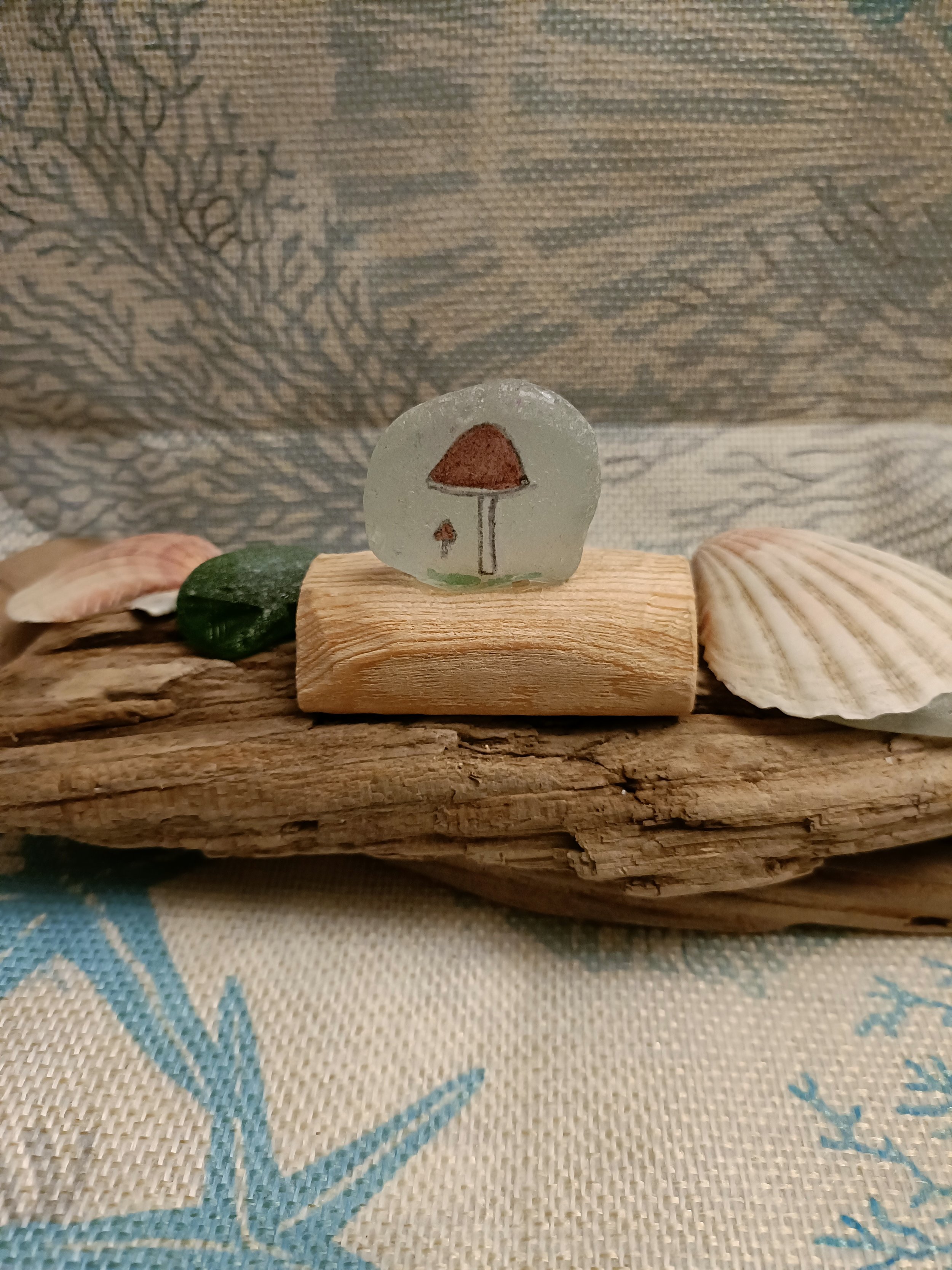 Painted sea glass with mushroom design on driftwood display with seashells
