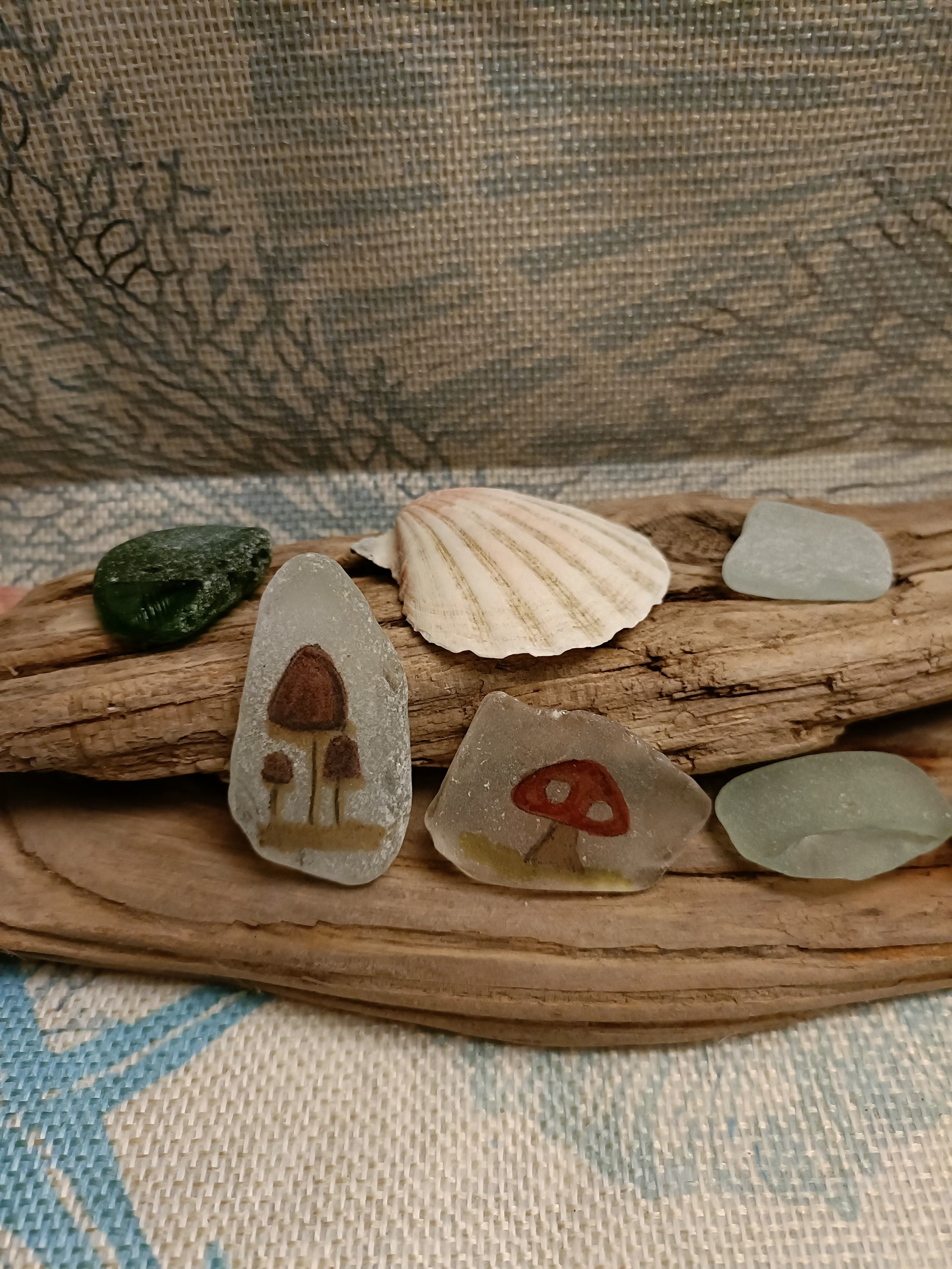 Decorative arrangement of seashells, driftwood, and sea glass with painted mushroom designs on glass.
