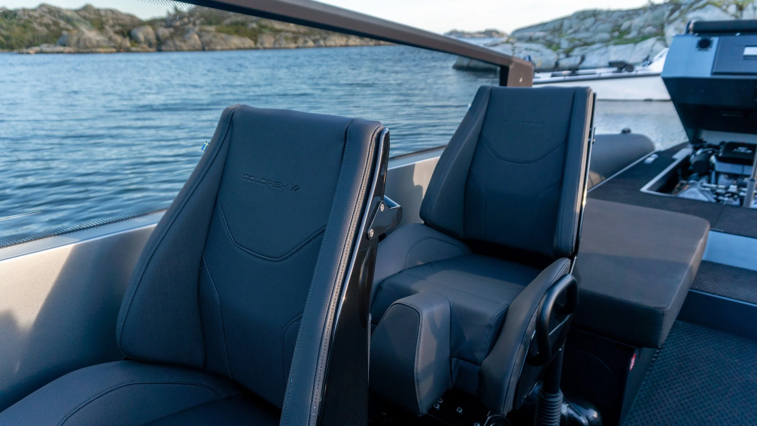 To svarte polstrede båtseter med tekst 'Golfstream V' på ryggsetet, inne i en båt med utsikt over vann og fjell.