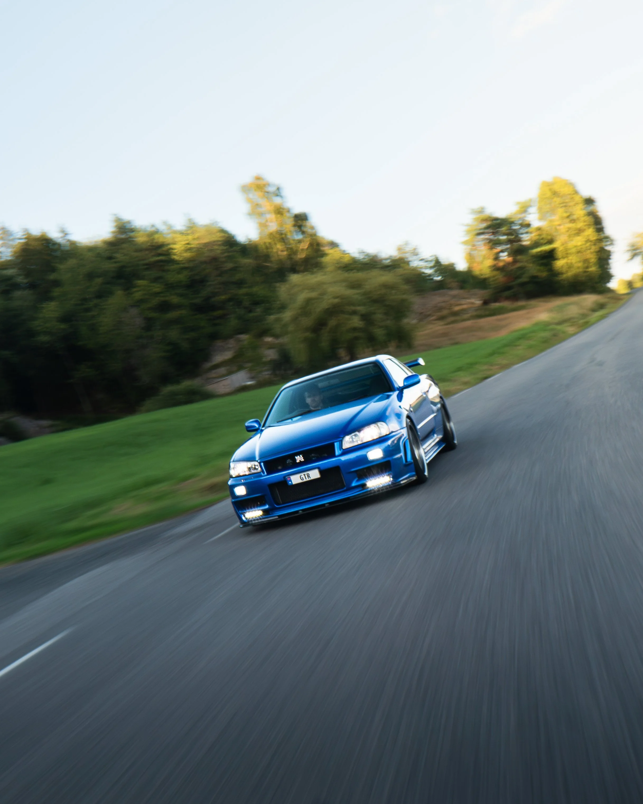 En blå sportsbil kjører raskt rundt en sving på en vei omringet av trær og gress.