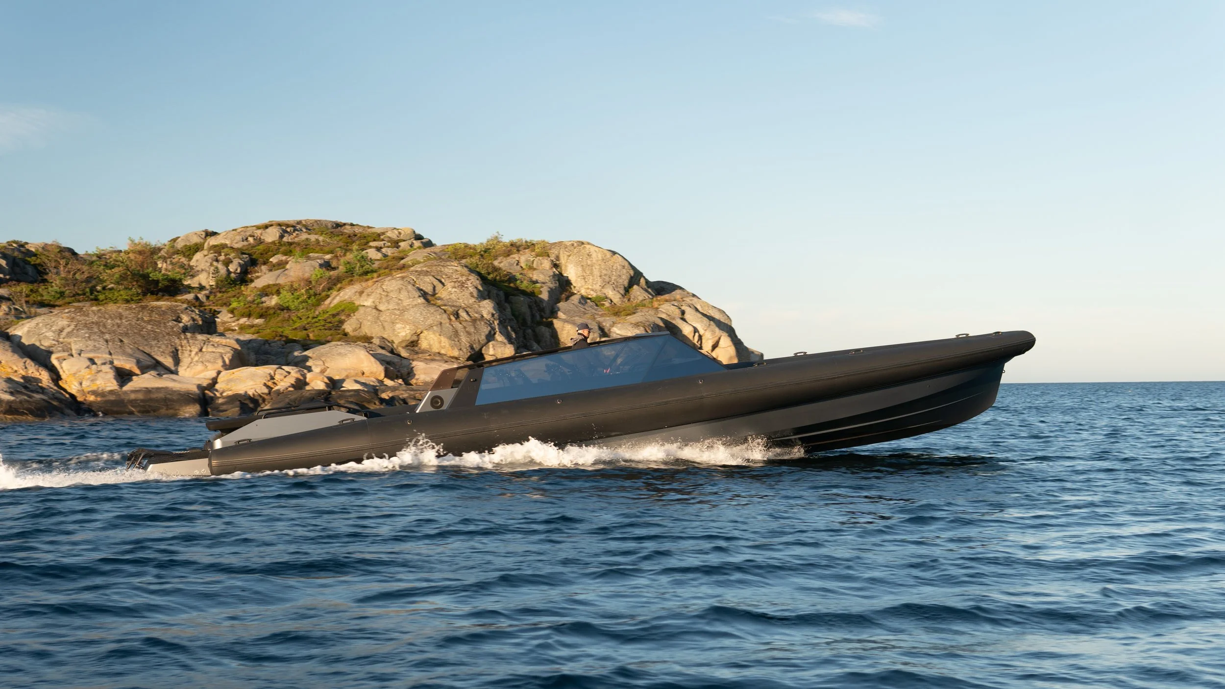 En svart motorbåt som kjører på åpne sjøen med klippeskråning i bakgrunnen.