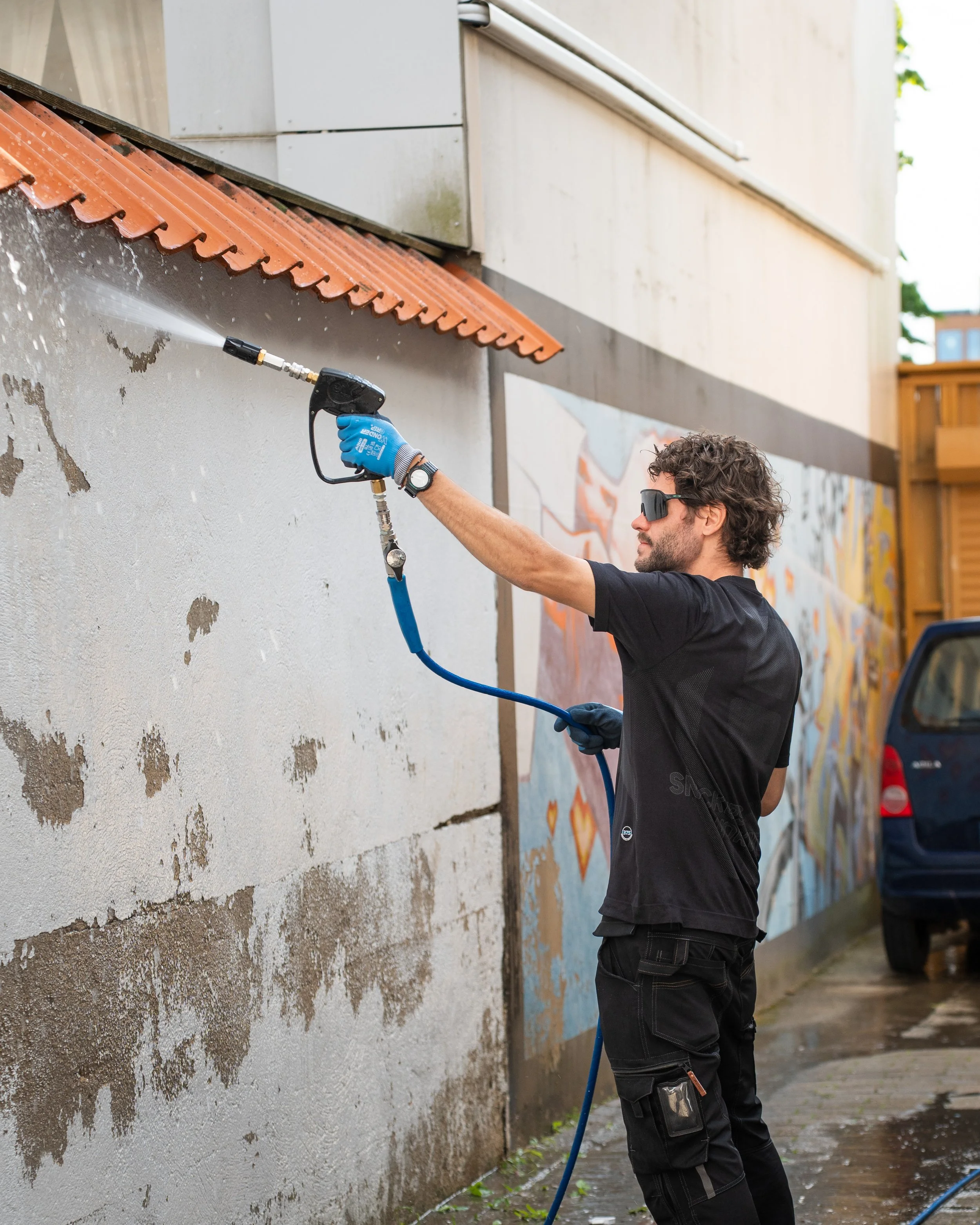Mann vasker en vegg med høytrykksspyler utendørs