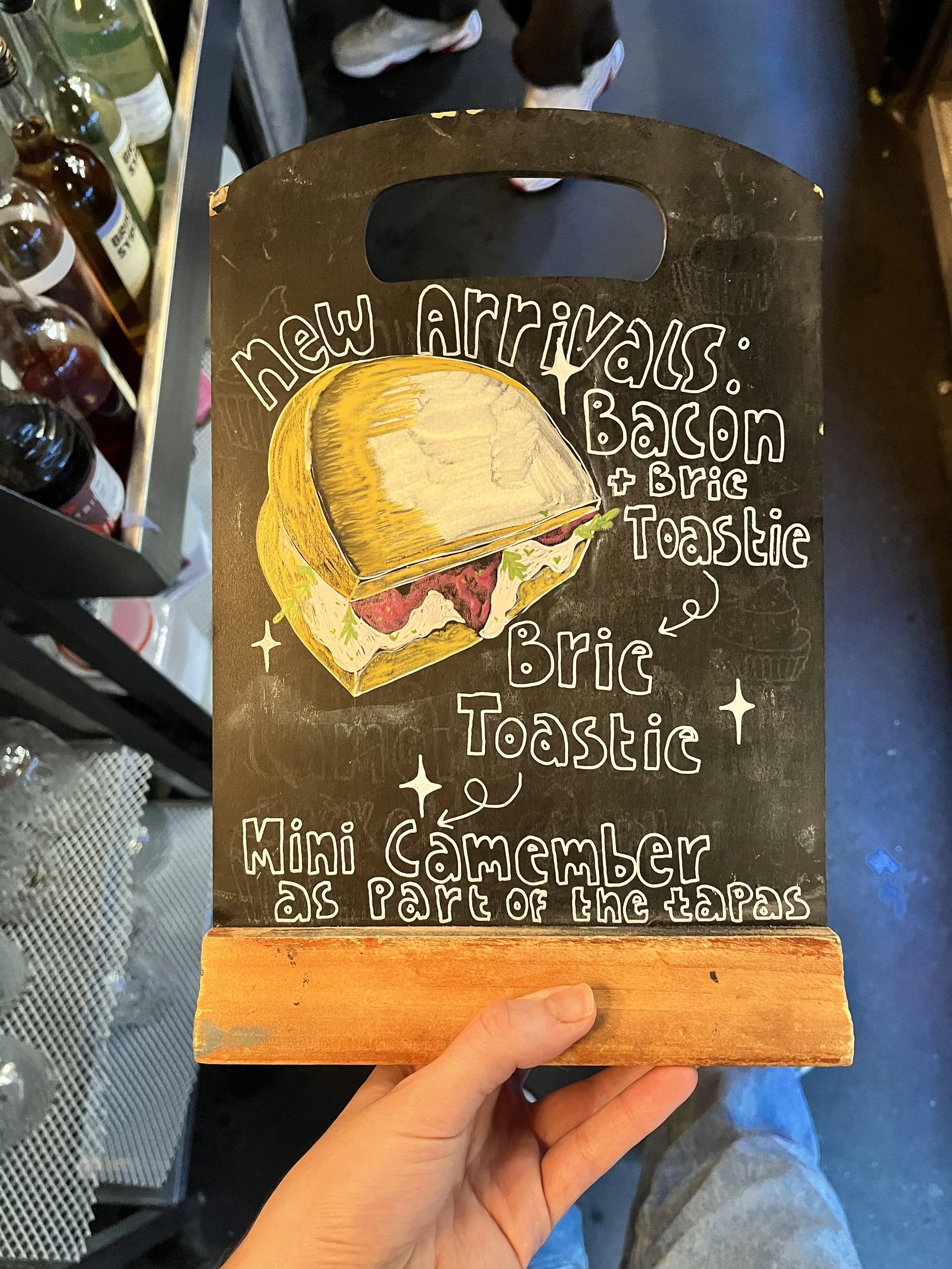 A4 sized Chalkboard promoting 'New Arrivals, including a selection of seasonal food'. Hand Drawn text + image using Posca Markers (2025).