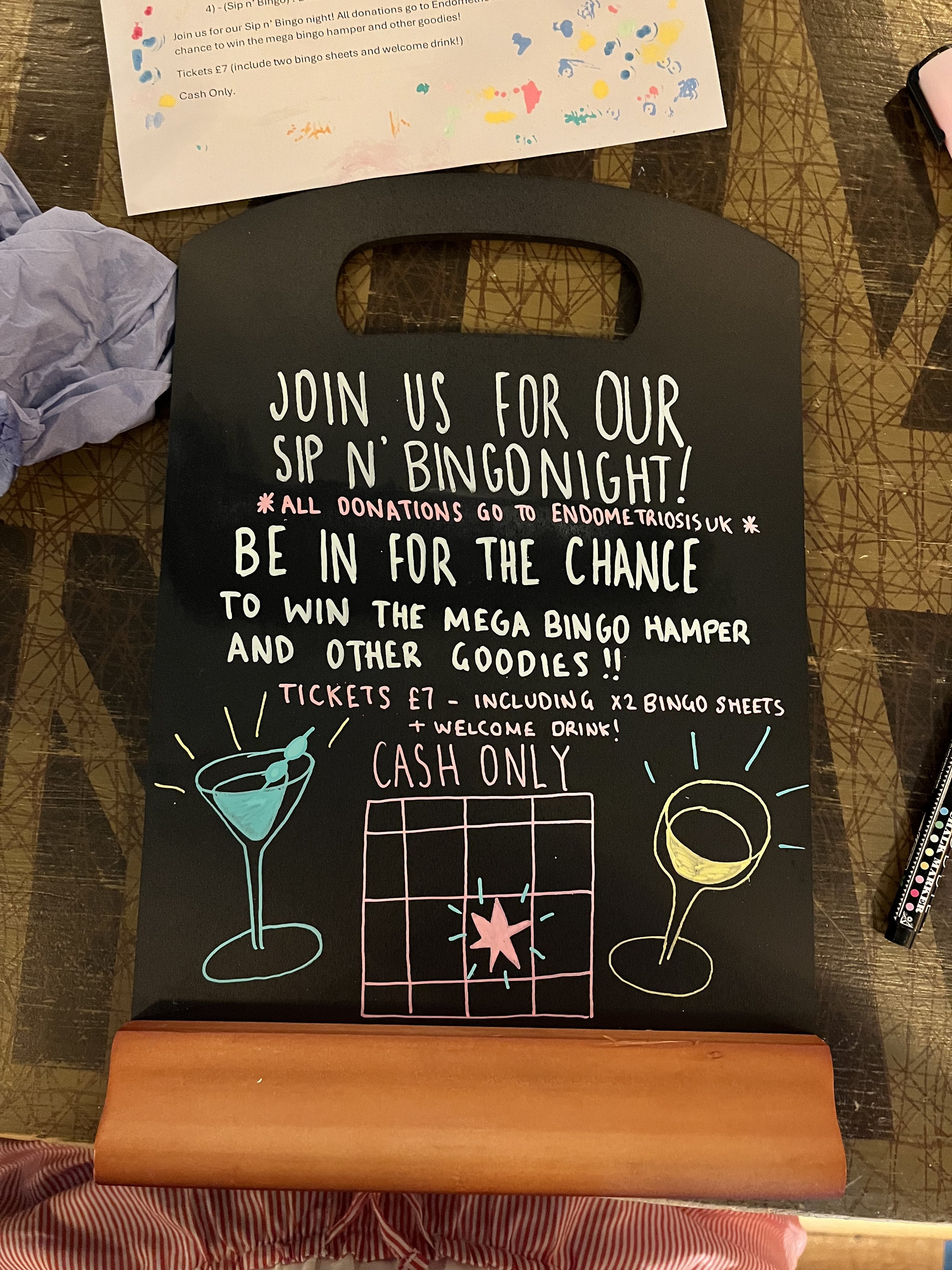 Chalkboard sign promoting Sip and Bingo Lounge Aid event, hand drawn text + image using Posca Pens (2025).