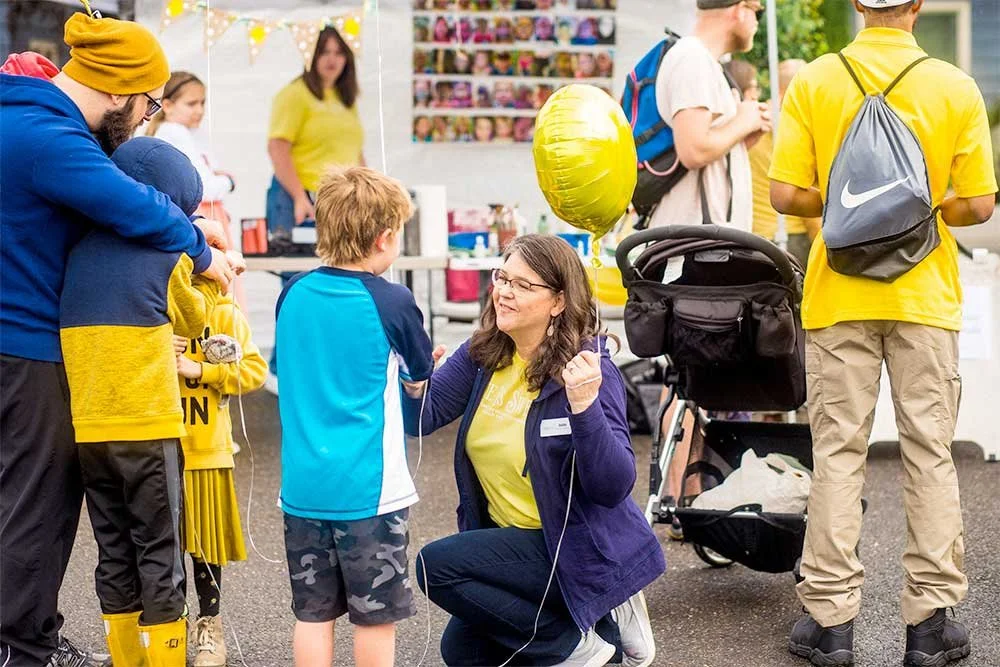 Woman kneeling talking to a child outdoors, holding a yellow balloon
