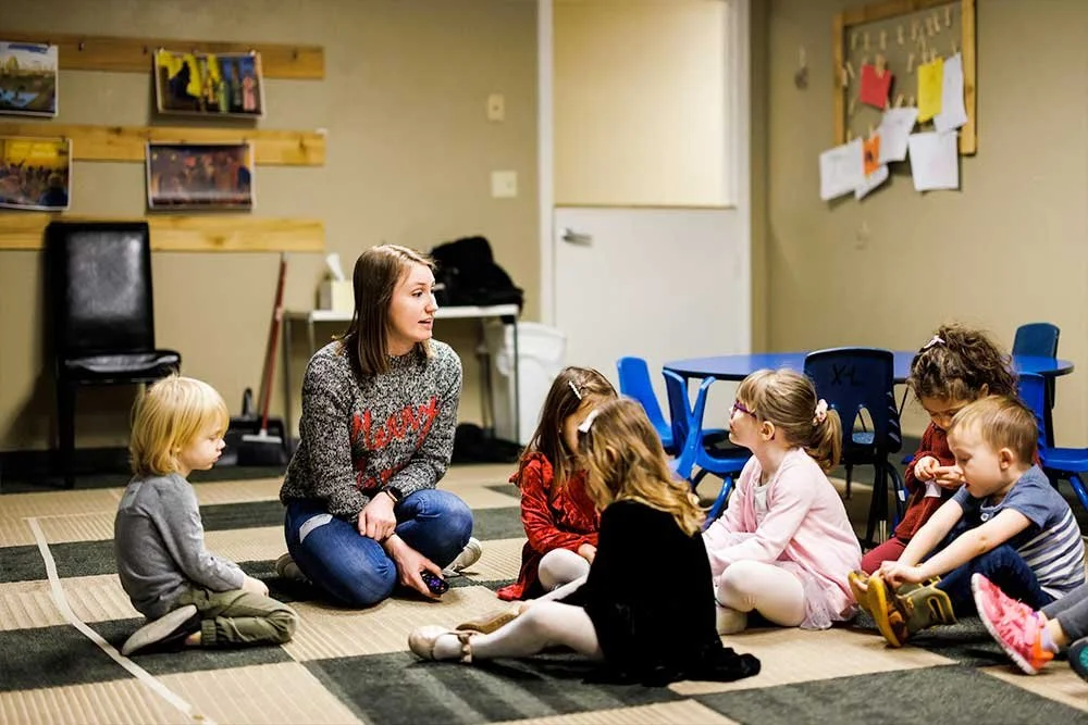 Woman kneeling and instructing preschoolers