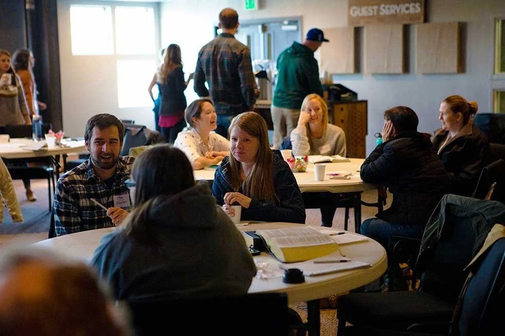 People chatting at tables in a classroom setting at a Harbor Curch event