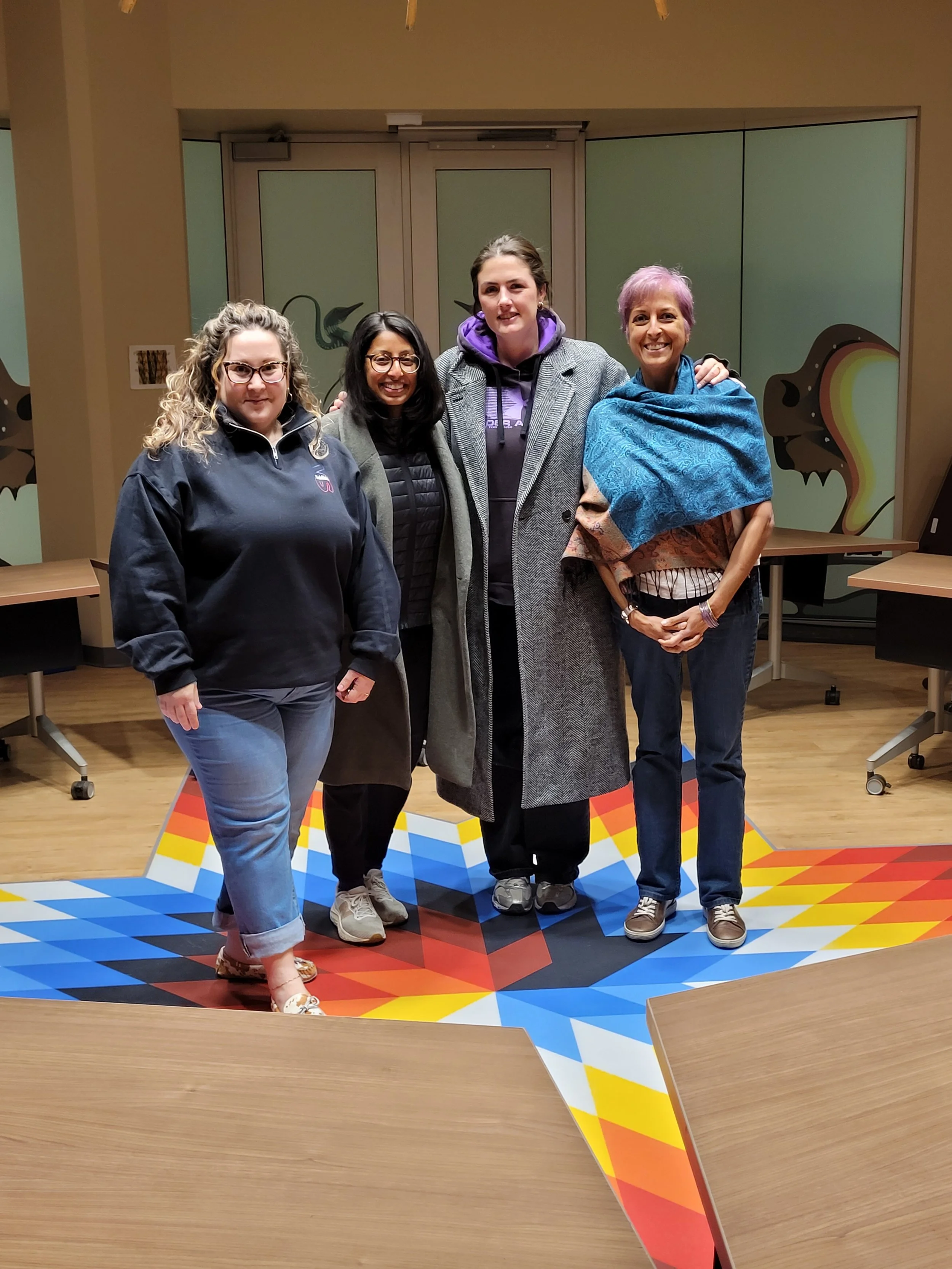 Four people standing together in a room with colorful geometric floor design and decorated walls.