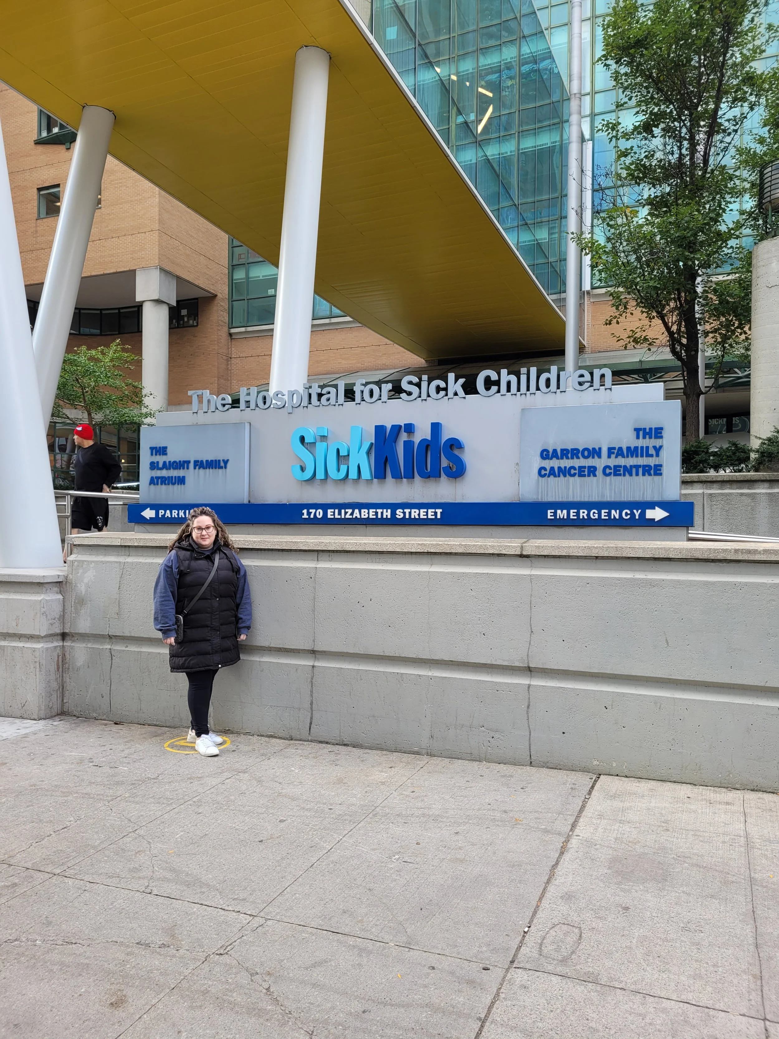 Sign for "The Hospital for Sick Children" and "SickKids" with people standing nearby.