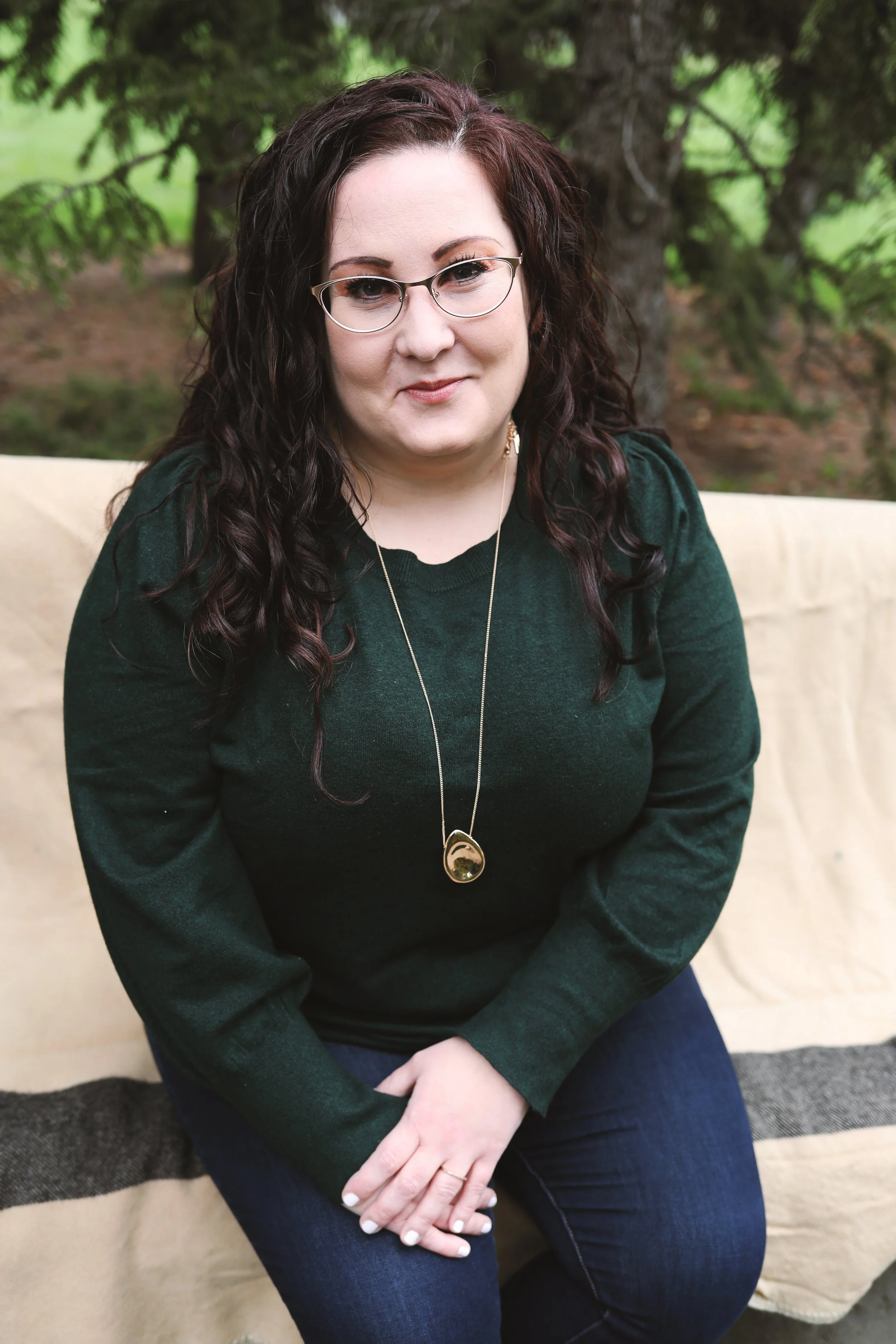Woman with glasses in green sweater sitting outdoors.