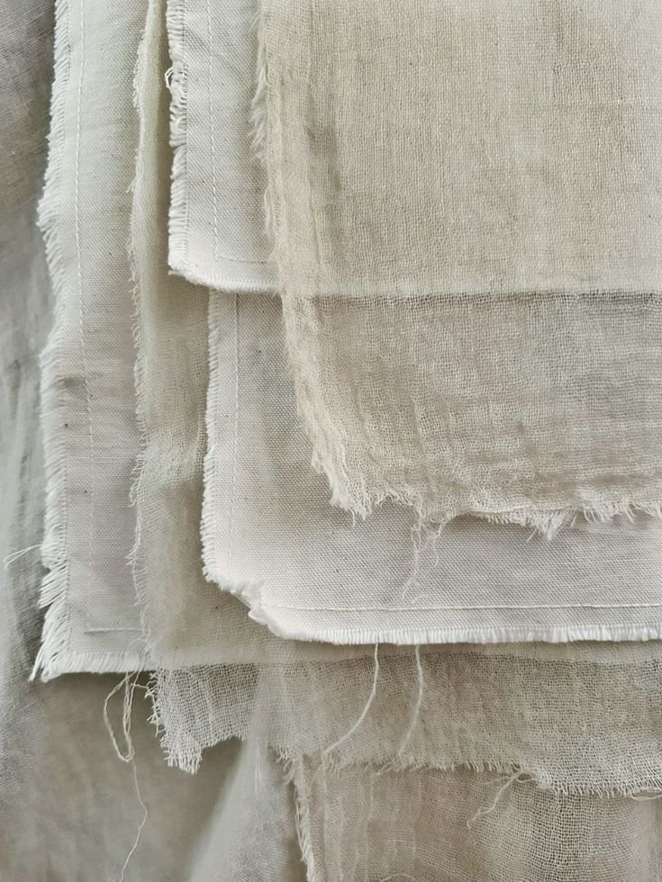 Close-up of multiple layers of off-white or cream-colored fabric with frayed edges, hanging or stacked together.