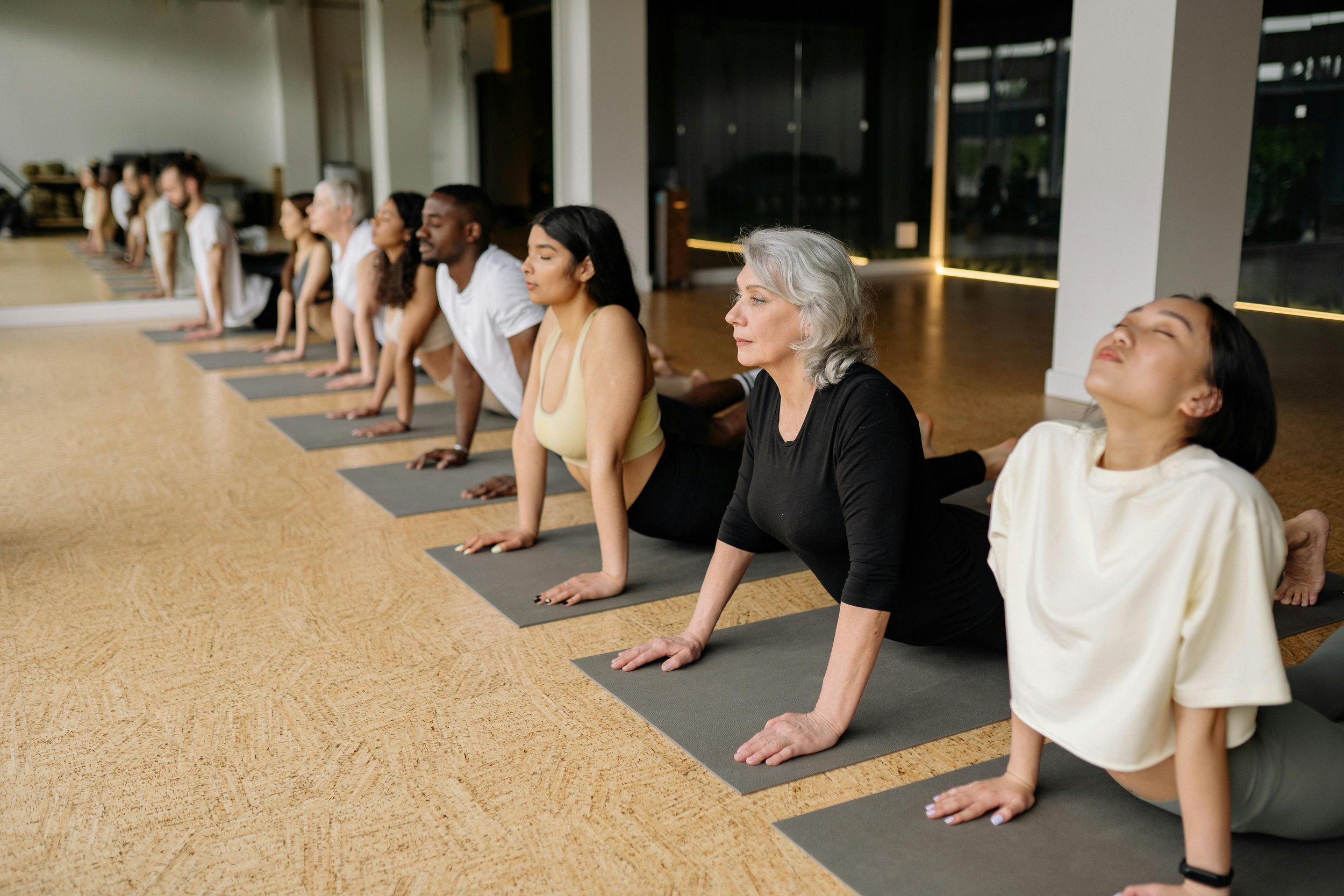 A diverse group of people practicing yoga in a studio, performing a pose on black yoga mats.