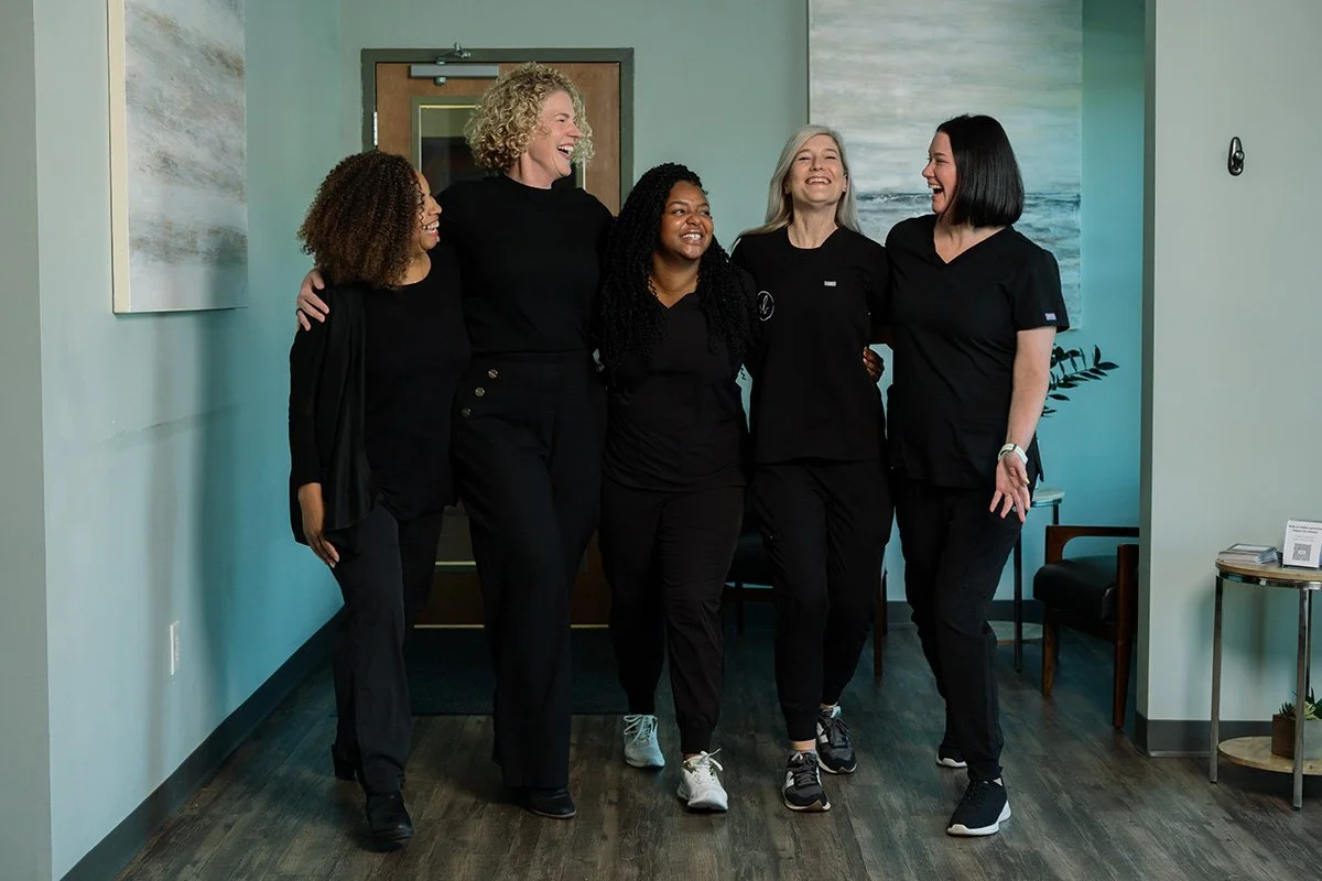 Group of five women in black scrubs walking and laughing together in a modern office.