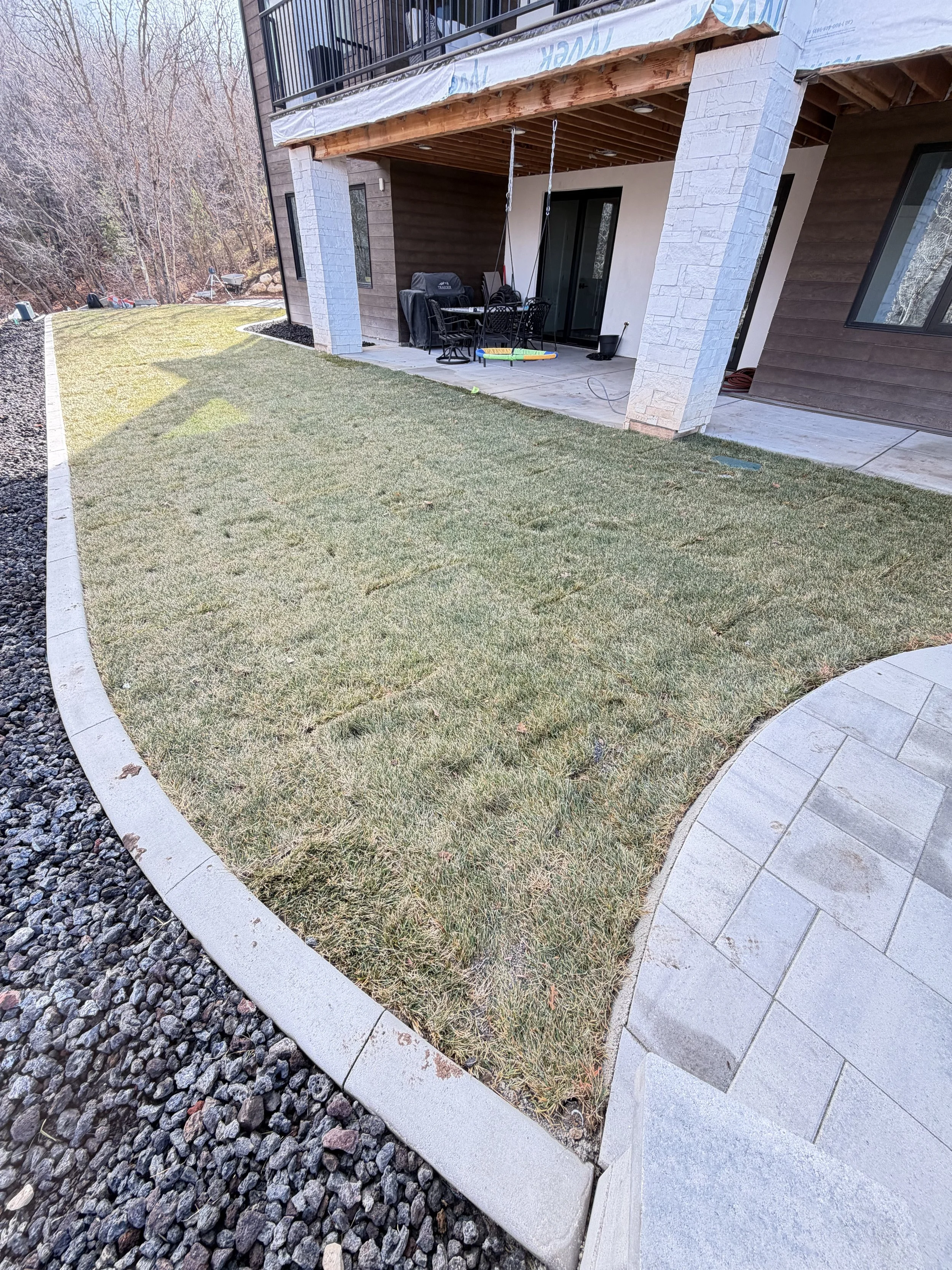 Completed backyard transformation in Woodland Hills Utah featuring fire pit, inground trampoline, grass and concrete features
