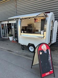 Kiosque à nourriture blanc avec une bannière ressemblant à un bandeau de nourriture, situé à l'extérieur sur le trottoir.