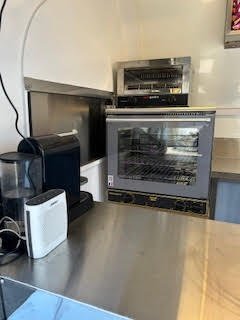 Four professionnel avec porte en verre, situé sur un comptoir en métal, entouré d'équipements électriques, dans une cuisine.