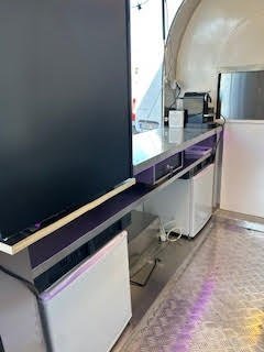 Vue d'une rangée de meubles et appareils électroniques dans un espace intérieur, avec un mur blanc incurvé et un sol en carrelage.