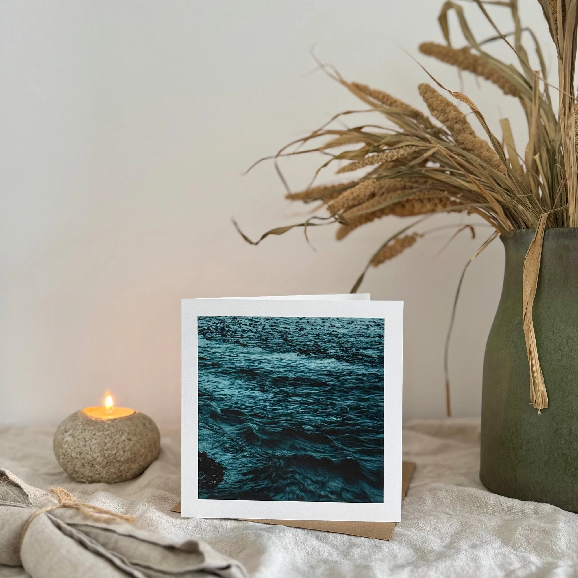 Water's Canvas greeting card styled with a stone candle and natural décor on a soft linen surface.