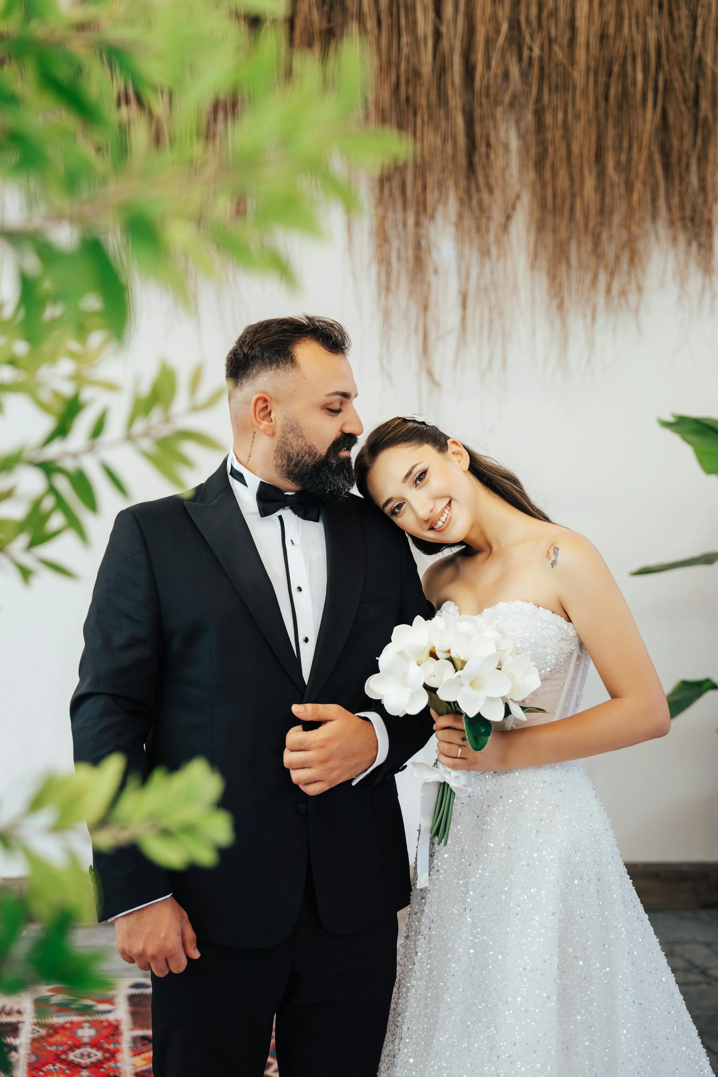 Bride and groom smiling on their wedding day surrounded by indoor plants and home-y decor.