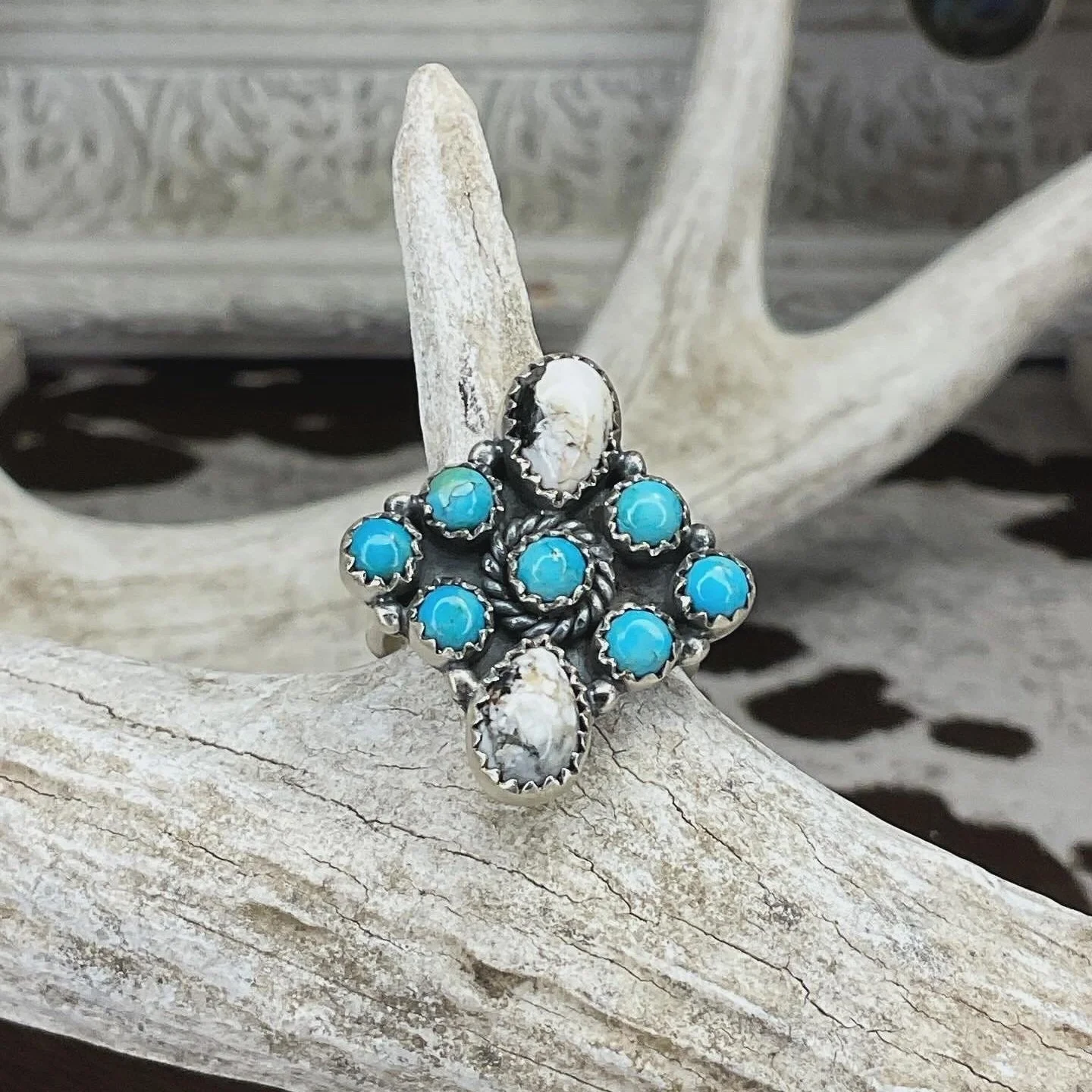 A silver ring with multiple blue turquoise stones and white coral accents, displayed on a piece of driftwood.