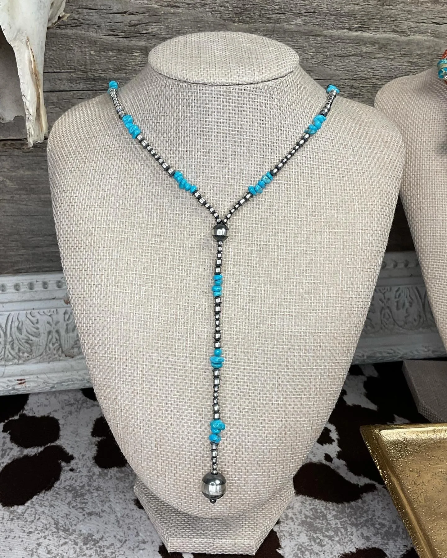 Coral-style necklace with turquoise and black beads, featuring a large silver bead pendant, displayed on a fabric necklace bust.