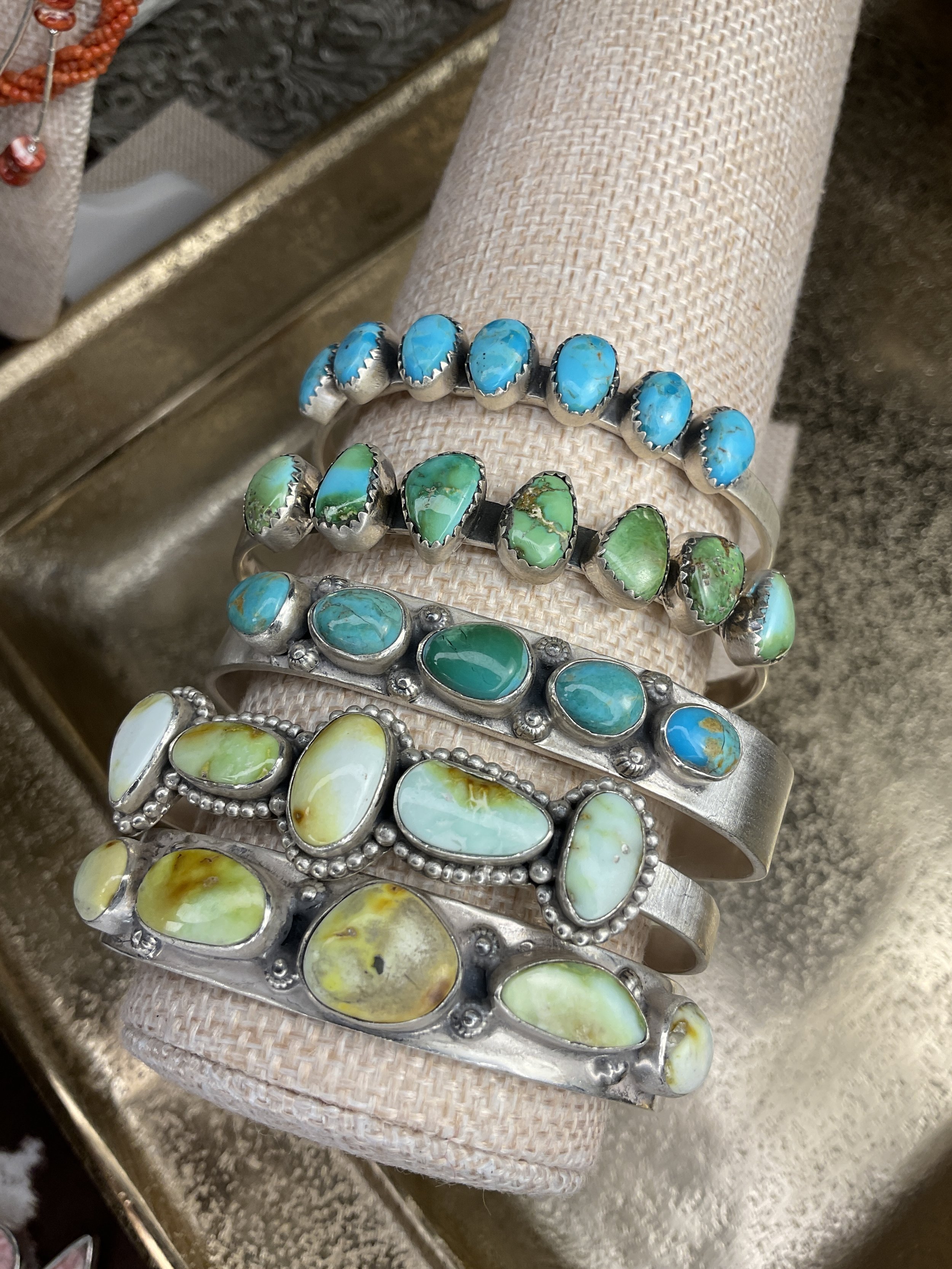 Four silver bracelets with turquoise and other colorful stones displayed on a pink fabric-covered jewelry holder.