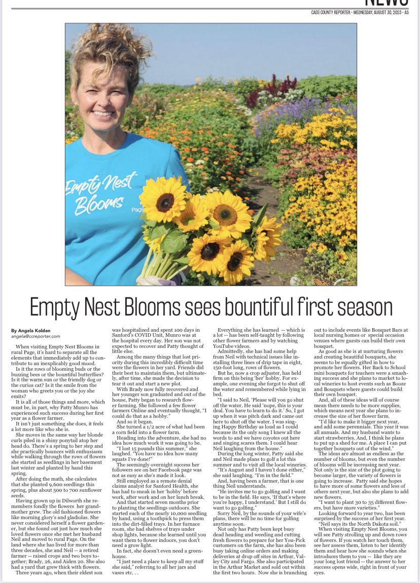 Woman holding a bouquet of sunflowers in a field of colorful flowers, smiling at the camera on a sunny day.