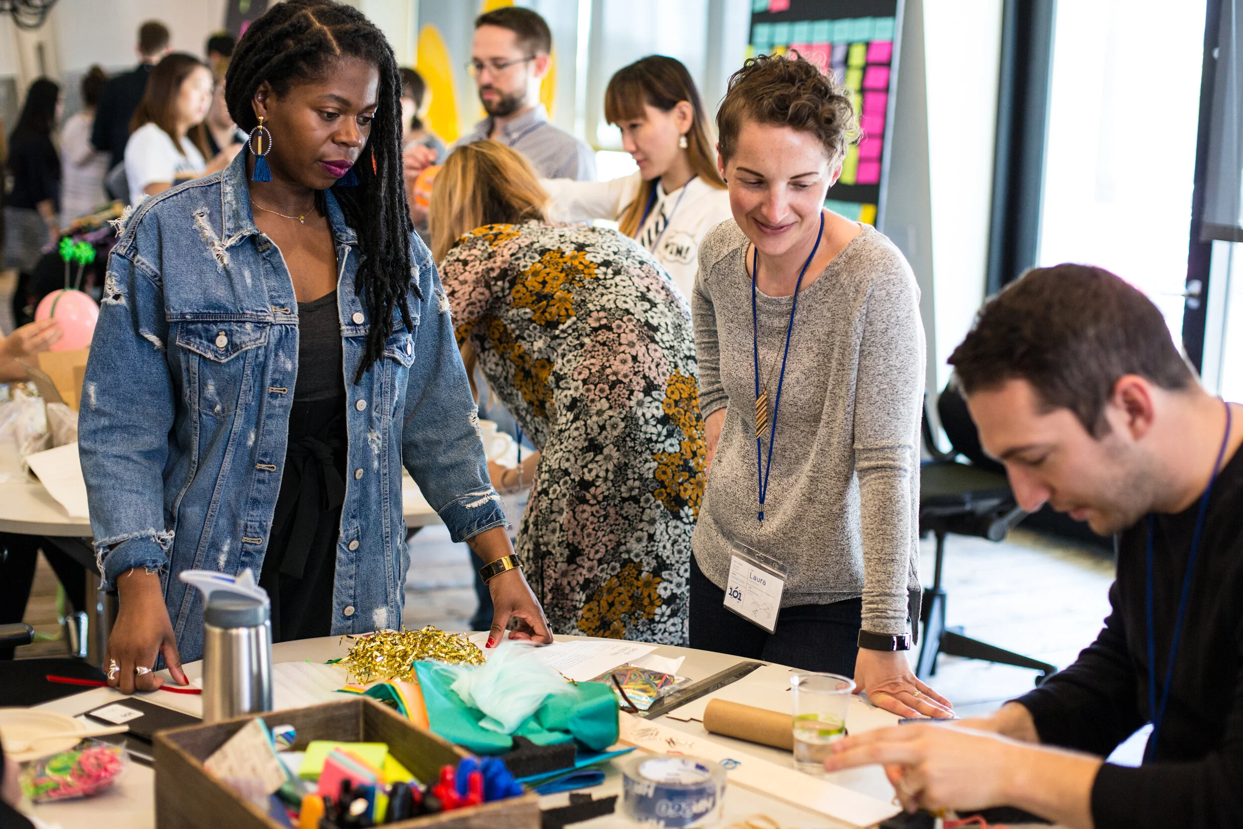 Women and men participating in a group activity at a workshop or seminar, with supplies and crafting materials on the table.