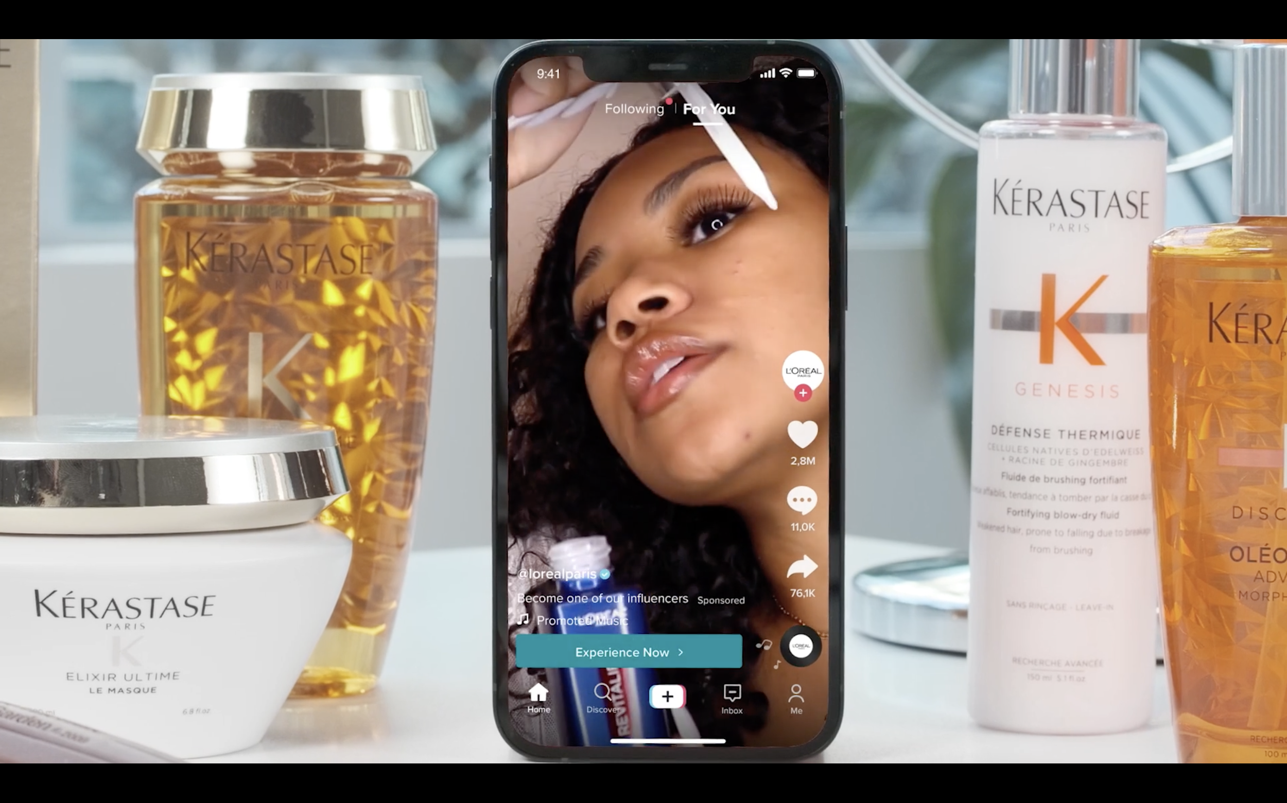 A smartphone displaying a TikTok video of a woman with curly hair and makeup surrounded by Kérastase hair care products, including shampoo, conditioner, and styling products.