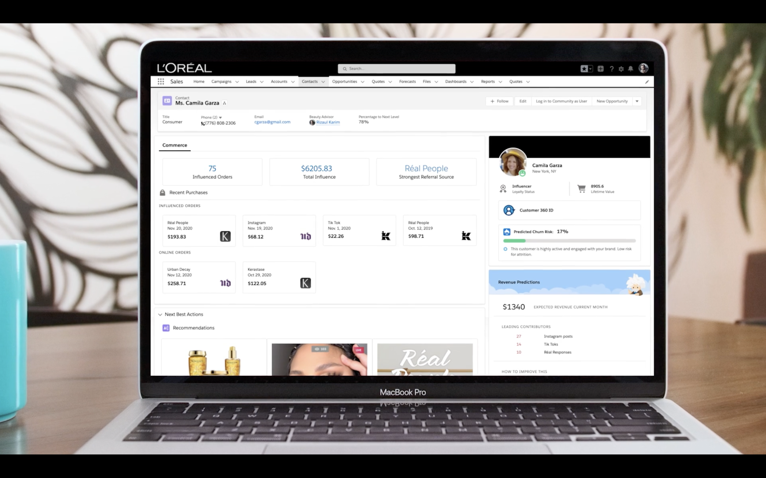 Open MacBook Pro displaying L'Oréal customer relationship management dashboard on a wooden desk with a teal mug on the left and a plant in the background.