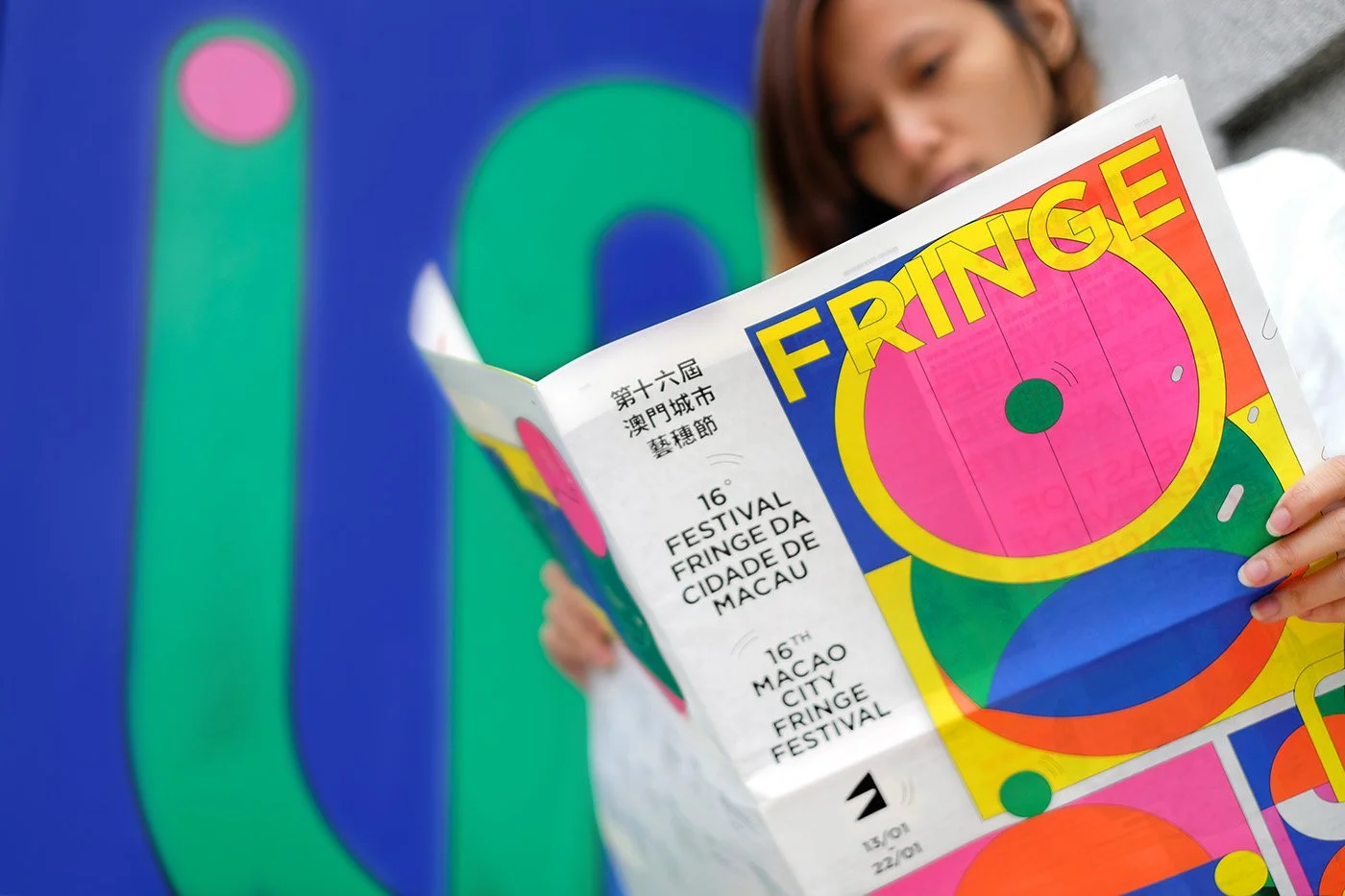 Person holding a colorful festival program with abstract artwork, indicating the 16th Macao City Fringe Festival.