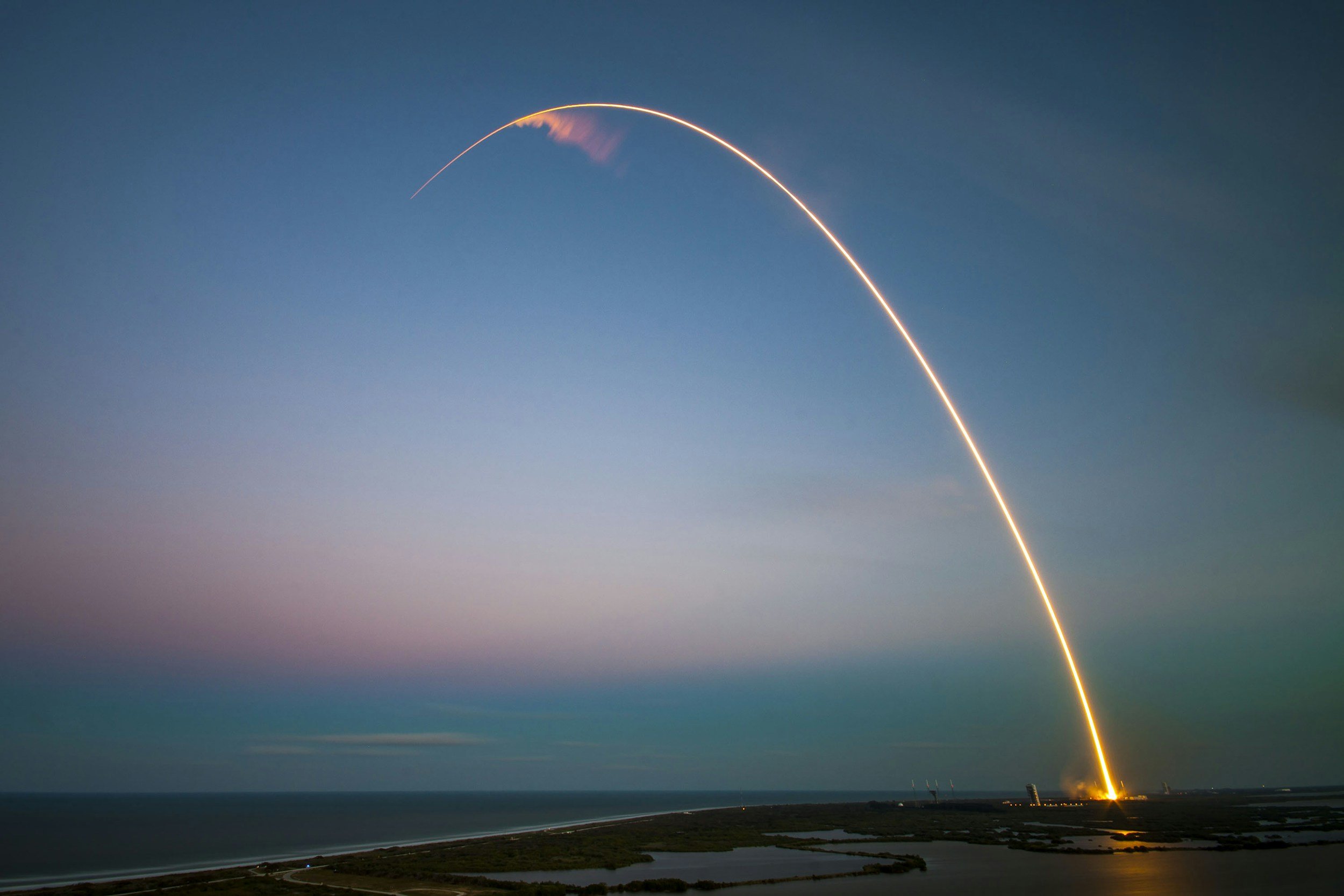 Long exposure of rocket launch over ocean at dusk.