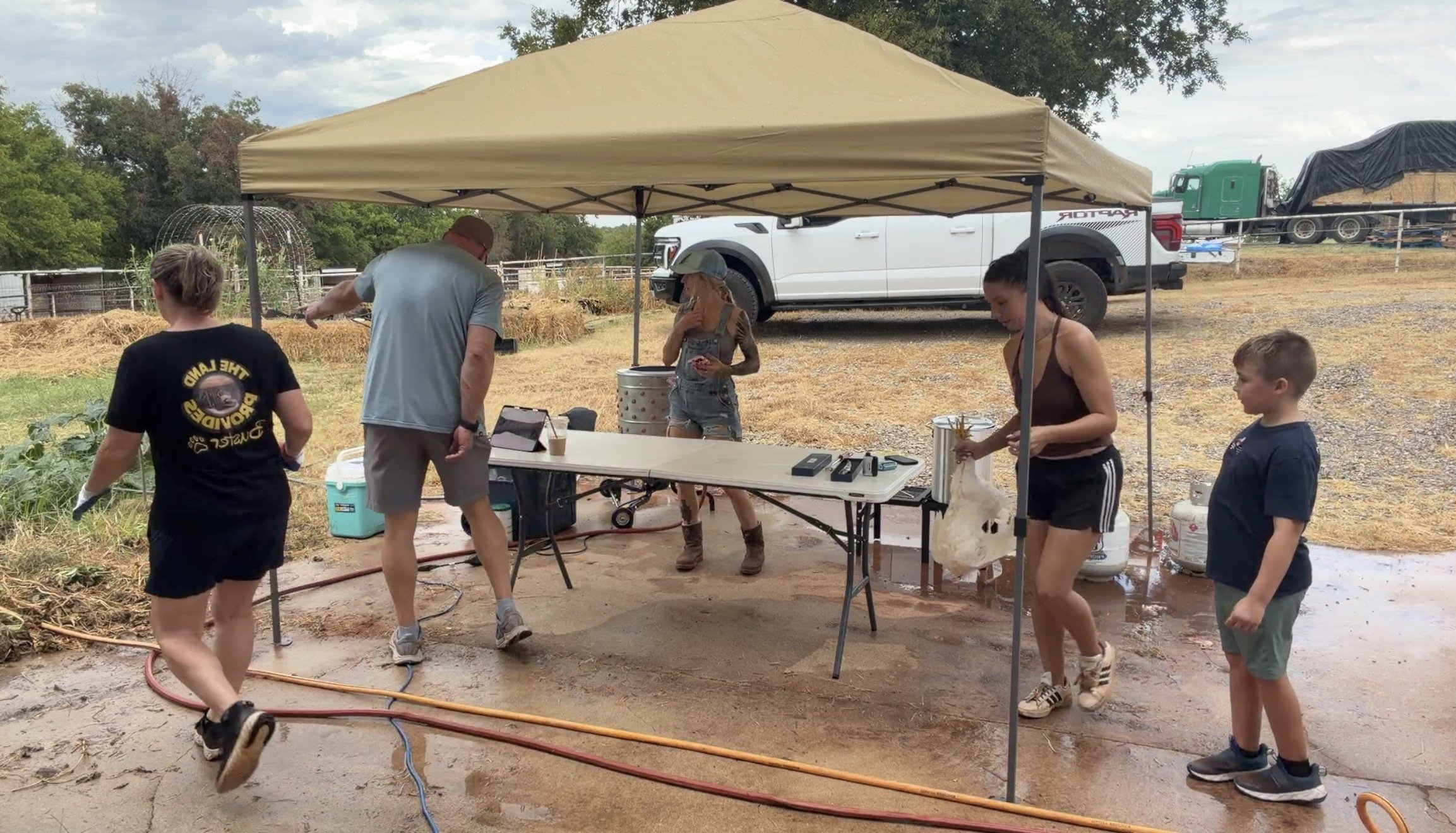A family outdoor under a pop up tent with chickens and chicken processing equipment