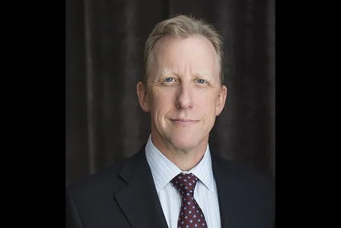 Professional man in a suit with a neutral expression, dark background.