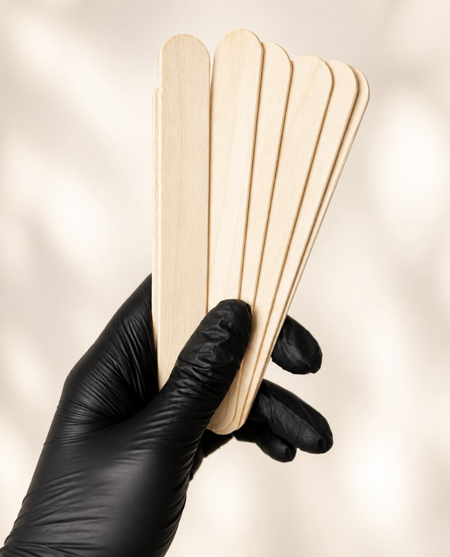 A hand wearing a black glove holding a bundle of light-colored wooden popsicle sticks.