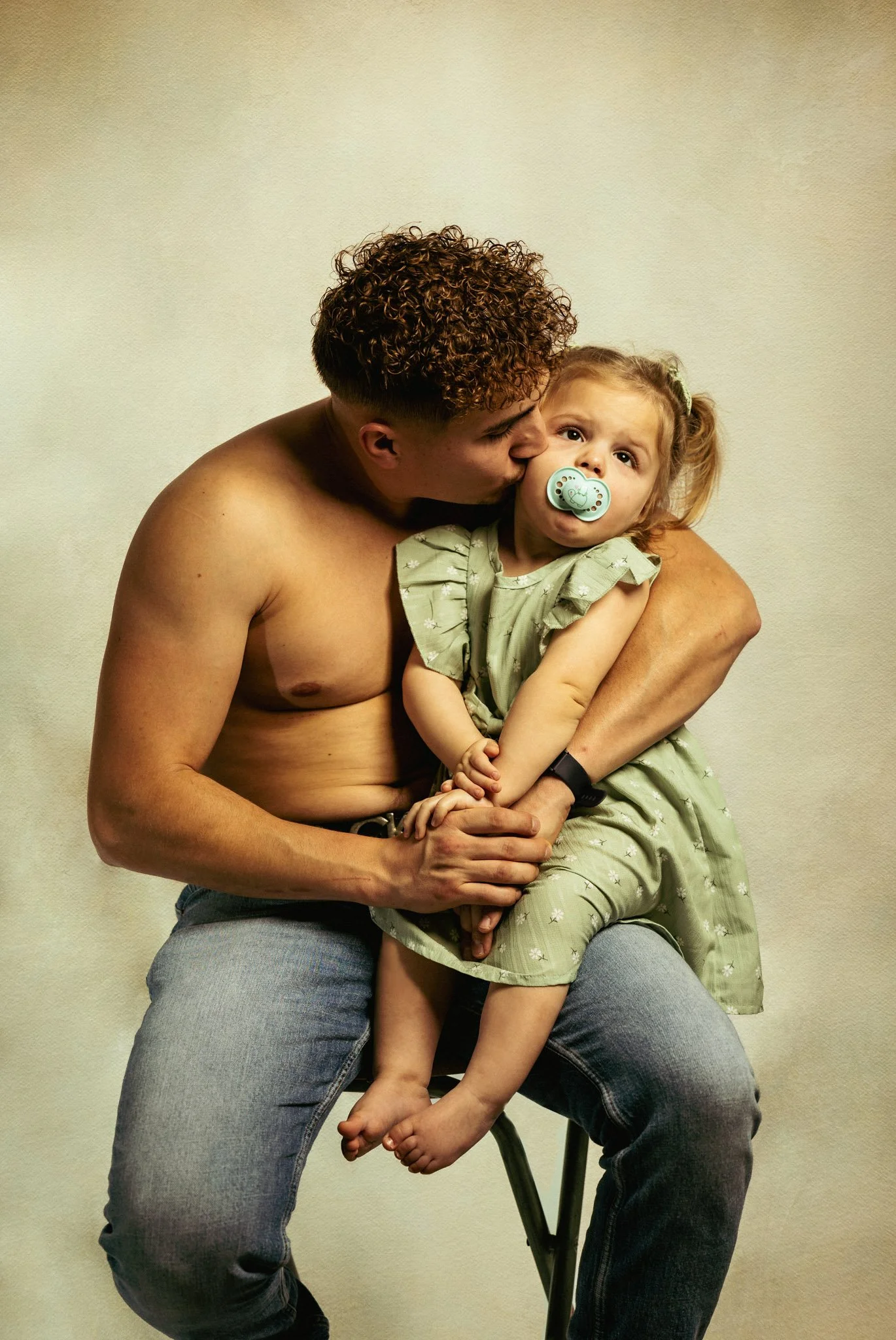 Photo de famille père et sa fille de 2 ans assis sur une chaise et bisou sur la joue