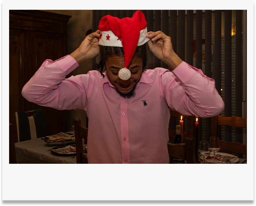 Photo style pola personne avec chemise rose qui enfile un bonnet de Père Noël